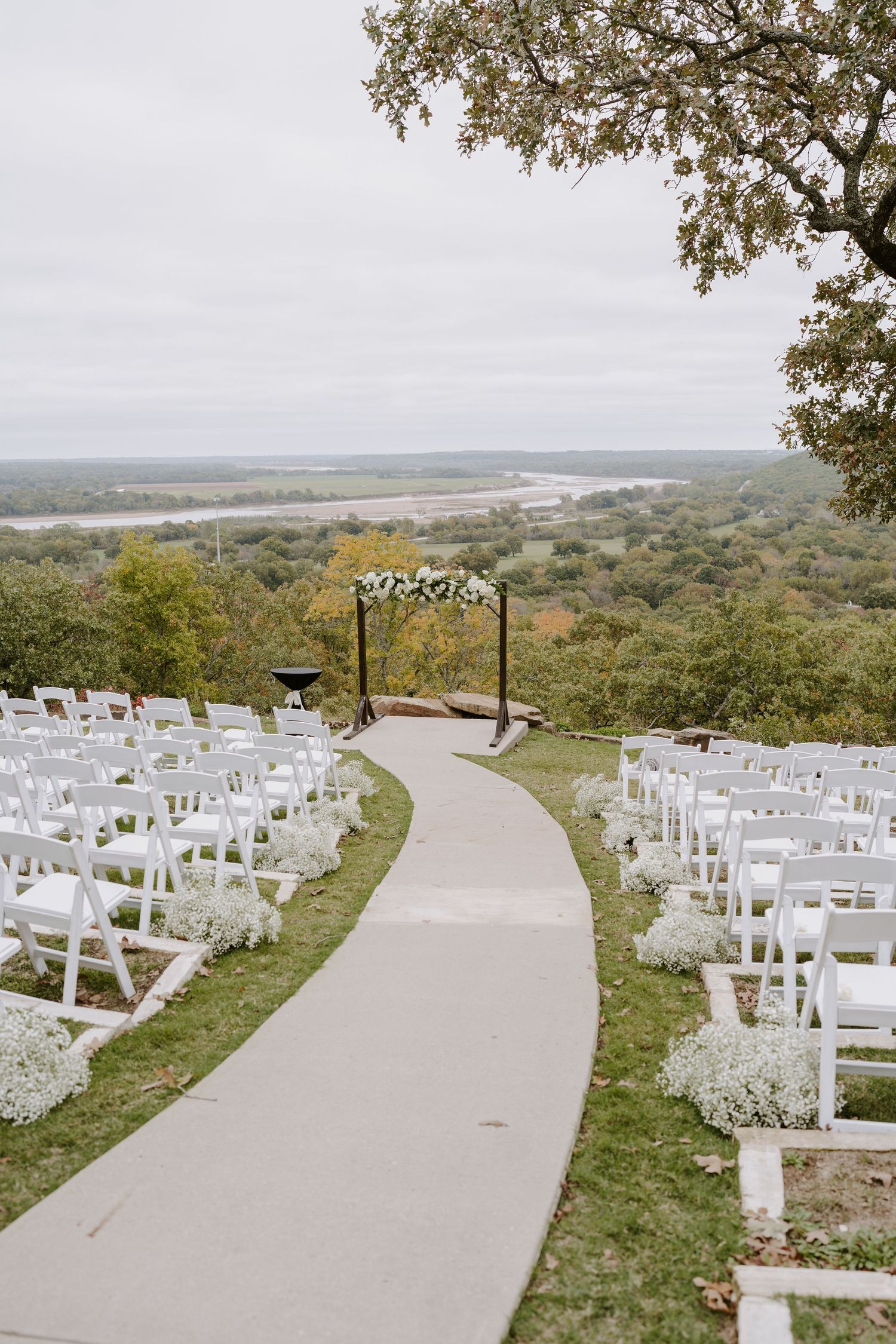 White ceremony chairs arranged along a curved pathway with scenic mountain views in the background.