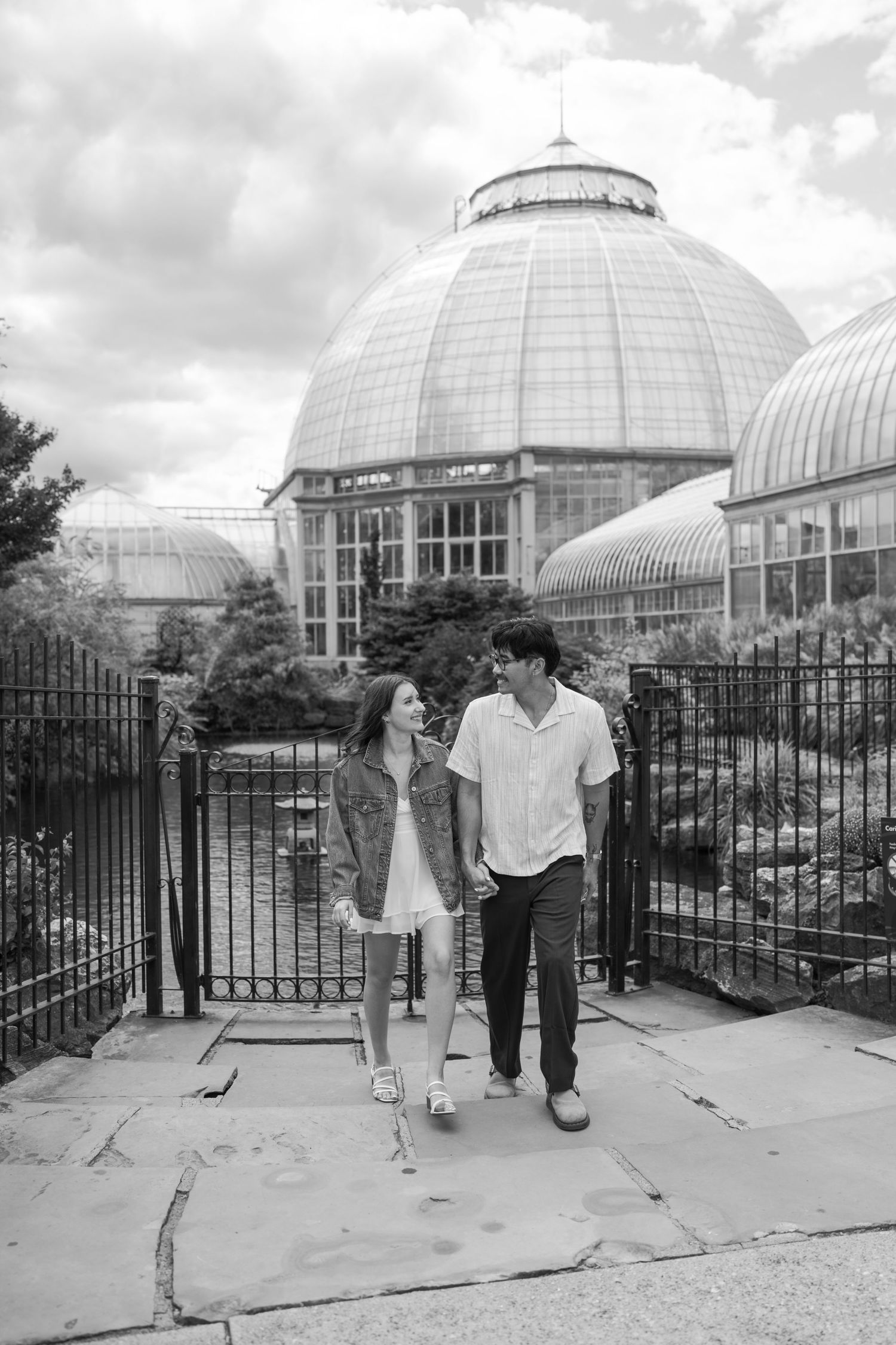 Black and white photo of couple standing by iron fence with domed conservatory building behind them.