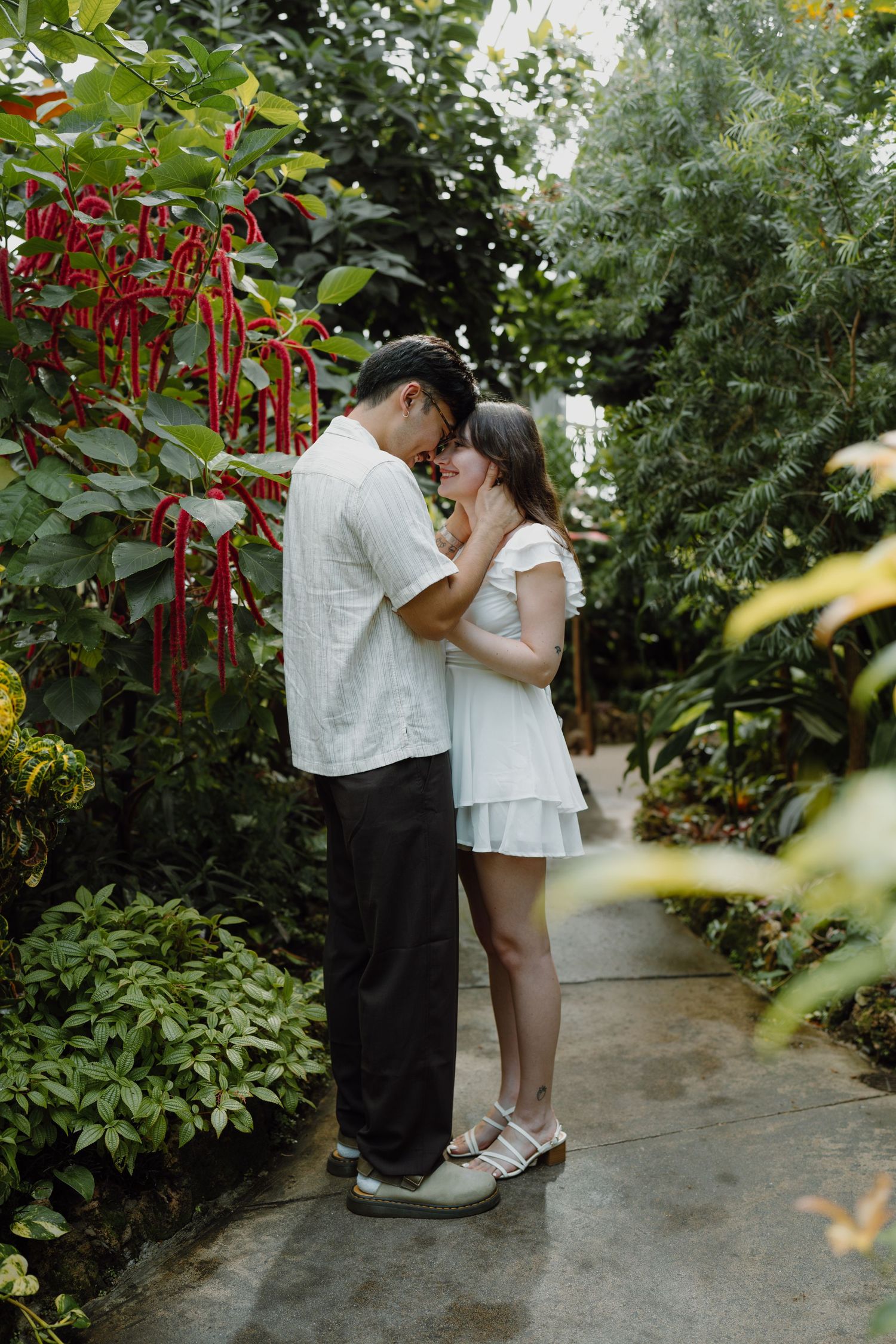 A couple shares romantic moments along a garden path with red flowers.