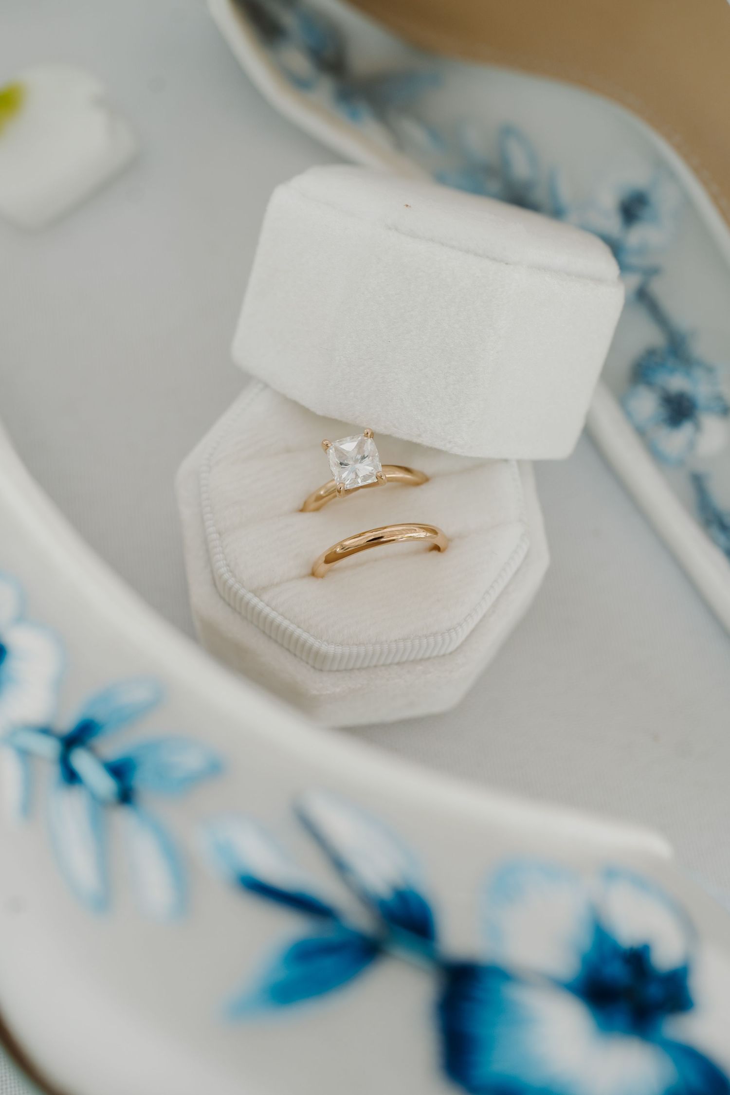 Delicate engagement ring displayed in a white octagonal ring box with blue floral accents.