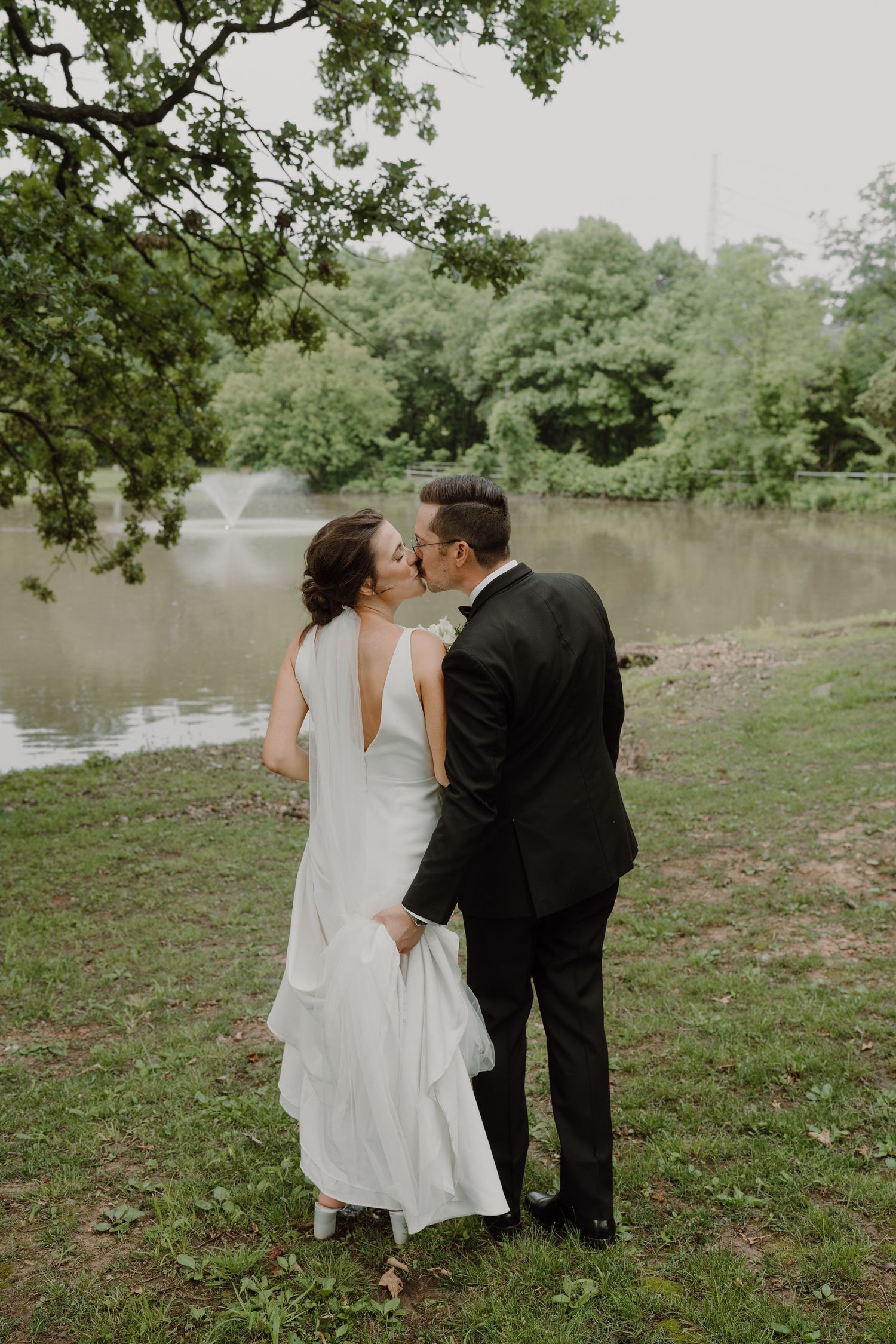 Wedding couple sharing intimate moments by a lakeside with lush greenery in the background.