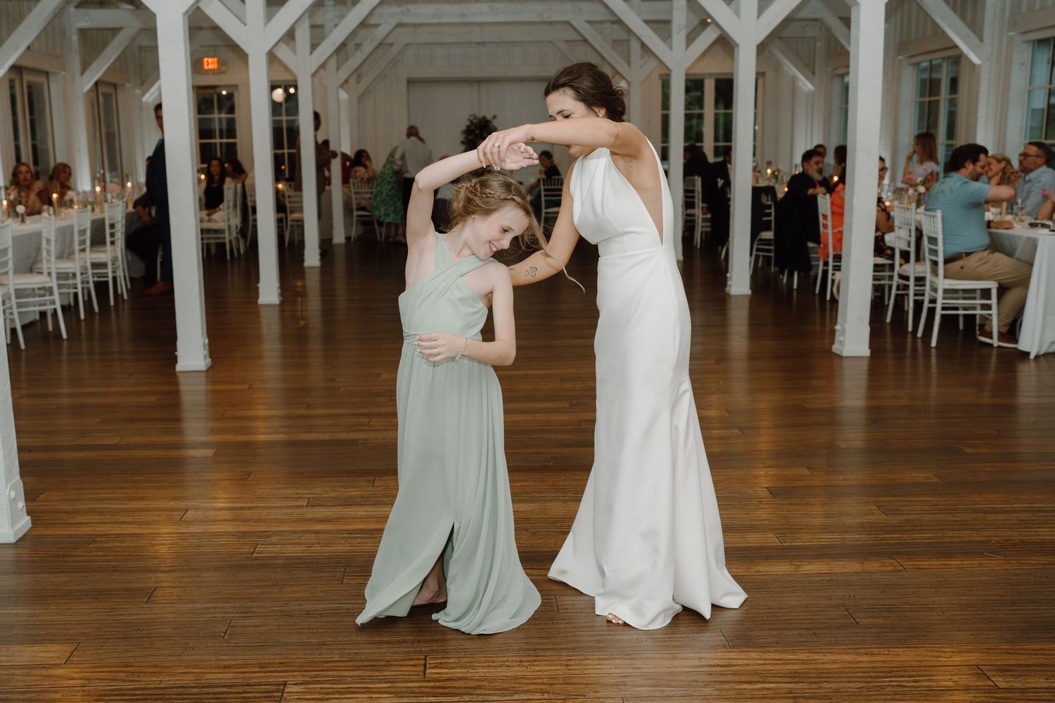 Wedding reception dance floor with guests celebrating in an elegant white barn-style venue.