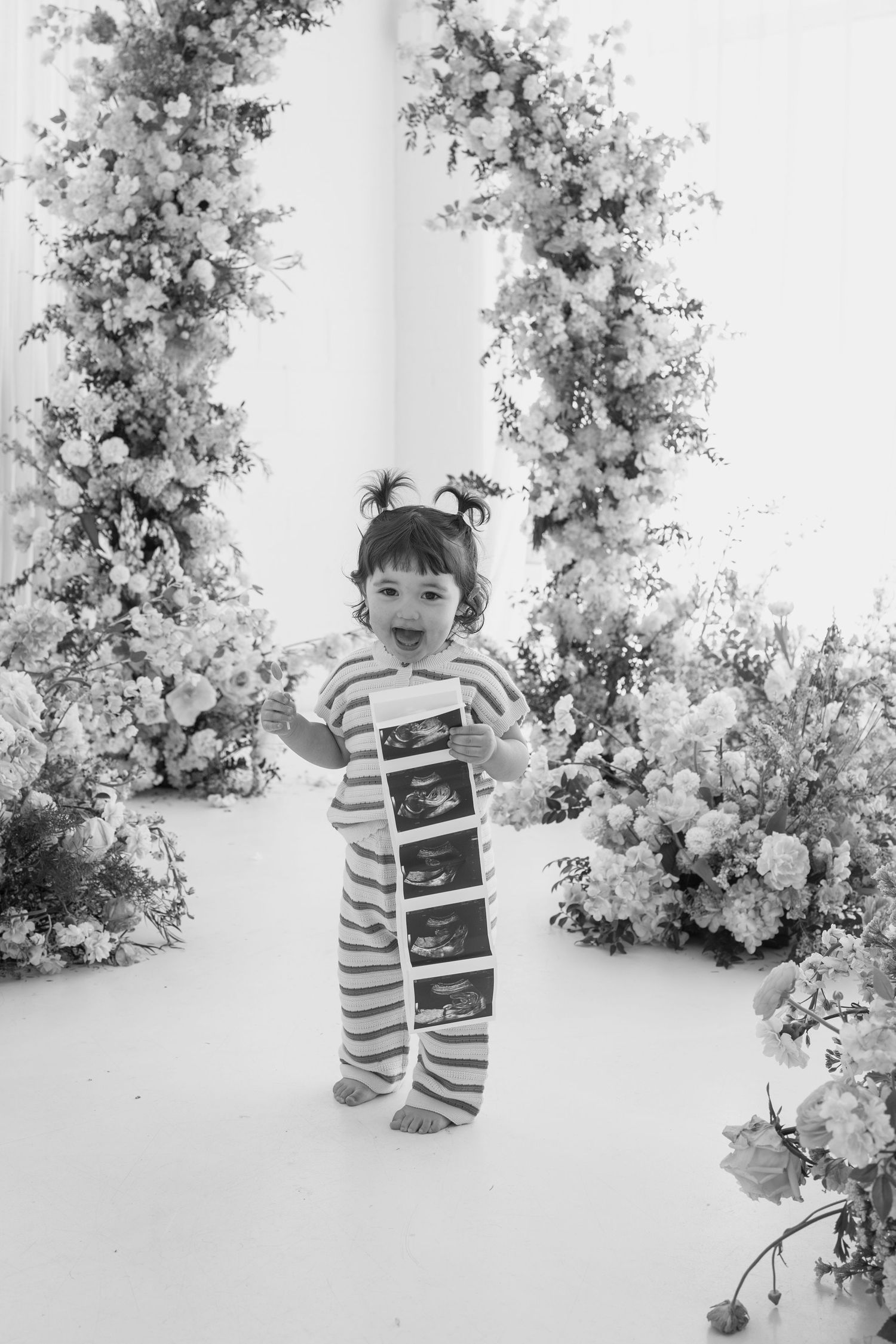 Black and white studio portrait with sonogram photos and floral arrangements.