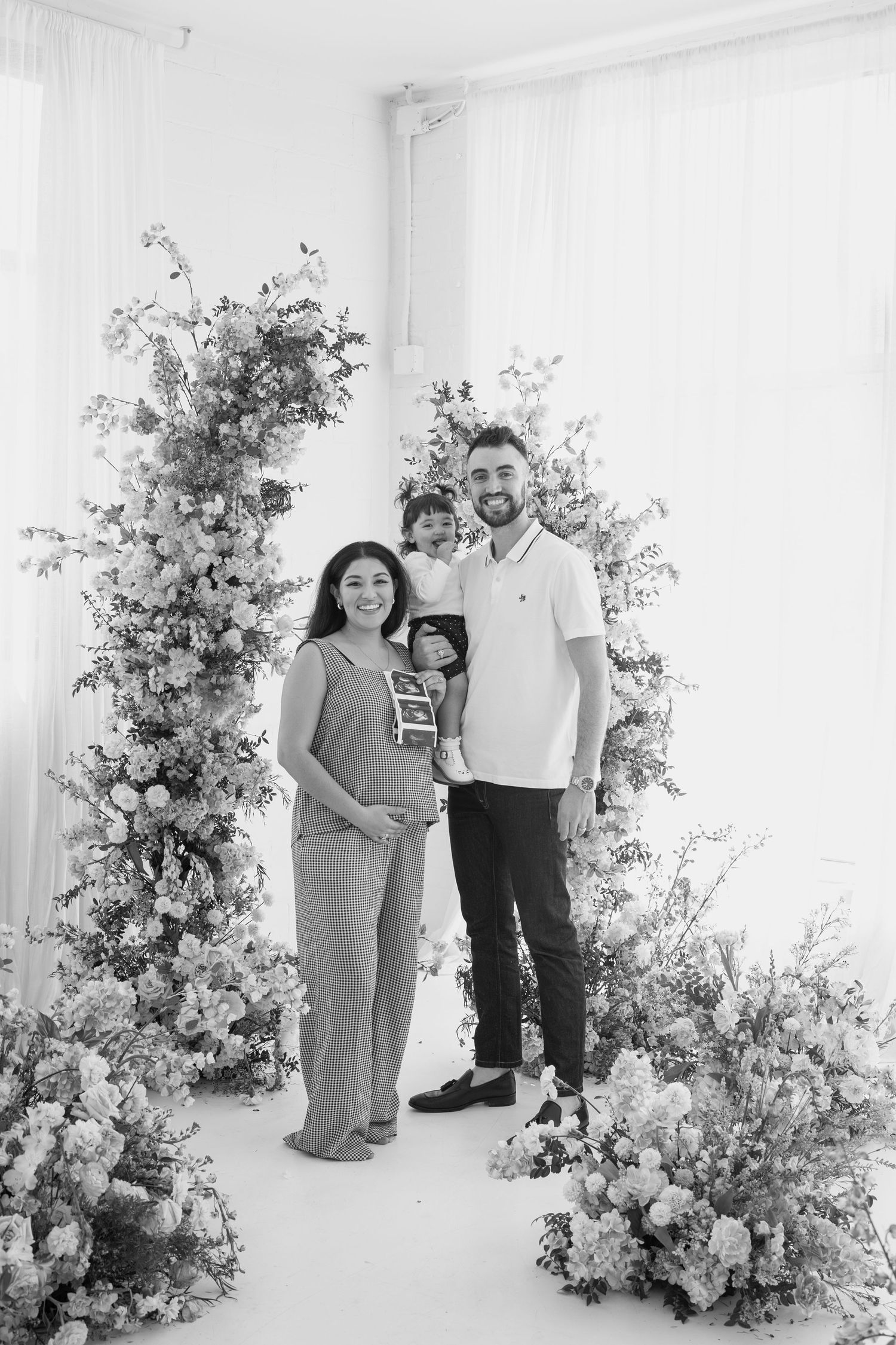 Black and white family portrait with elegant floral arrangements in a modern studio setting.