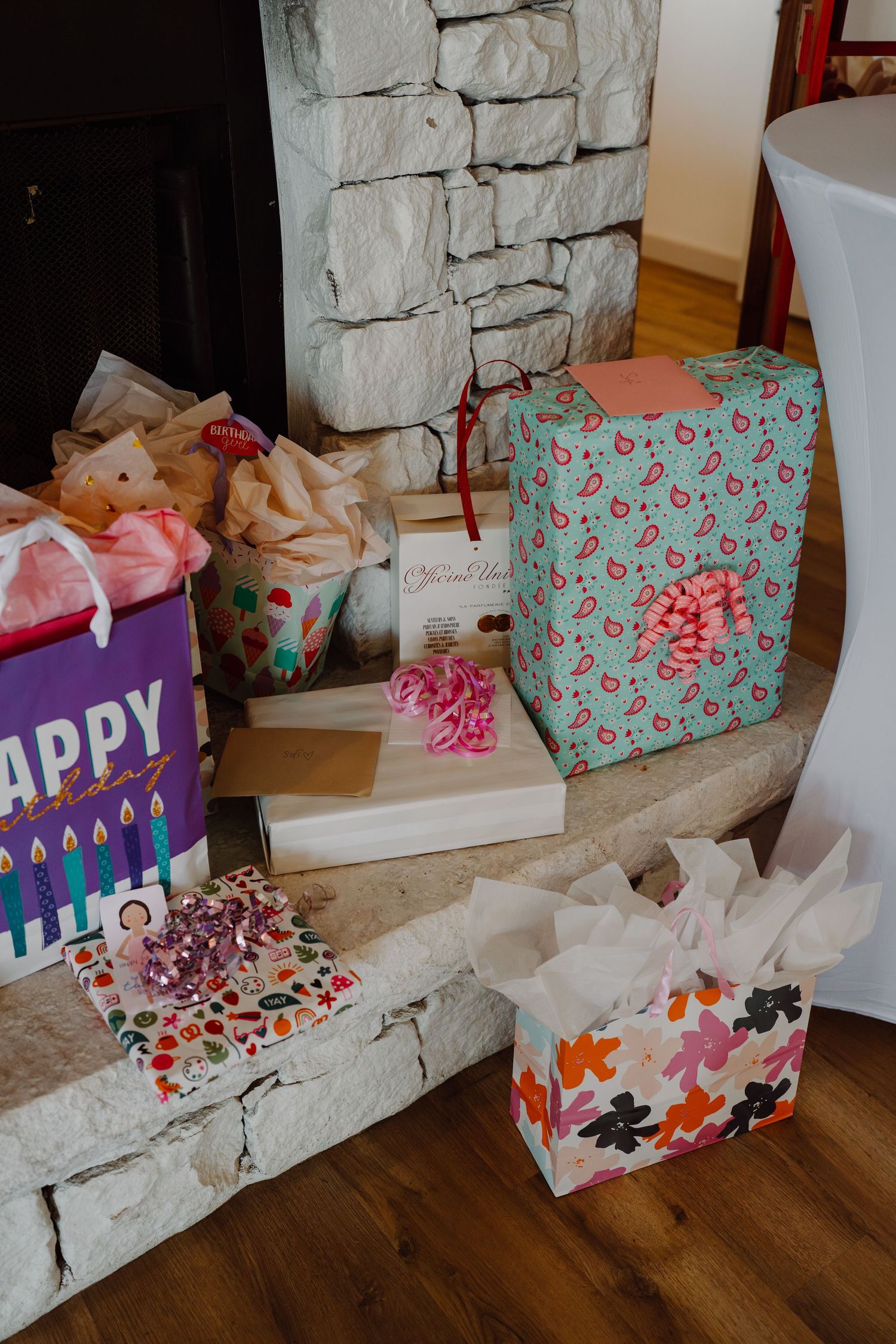 Festive gift bags and presents displayed along a stone fireplace mantel.