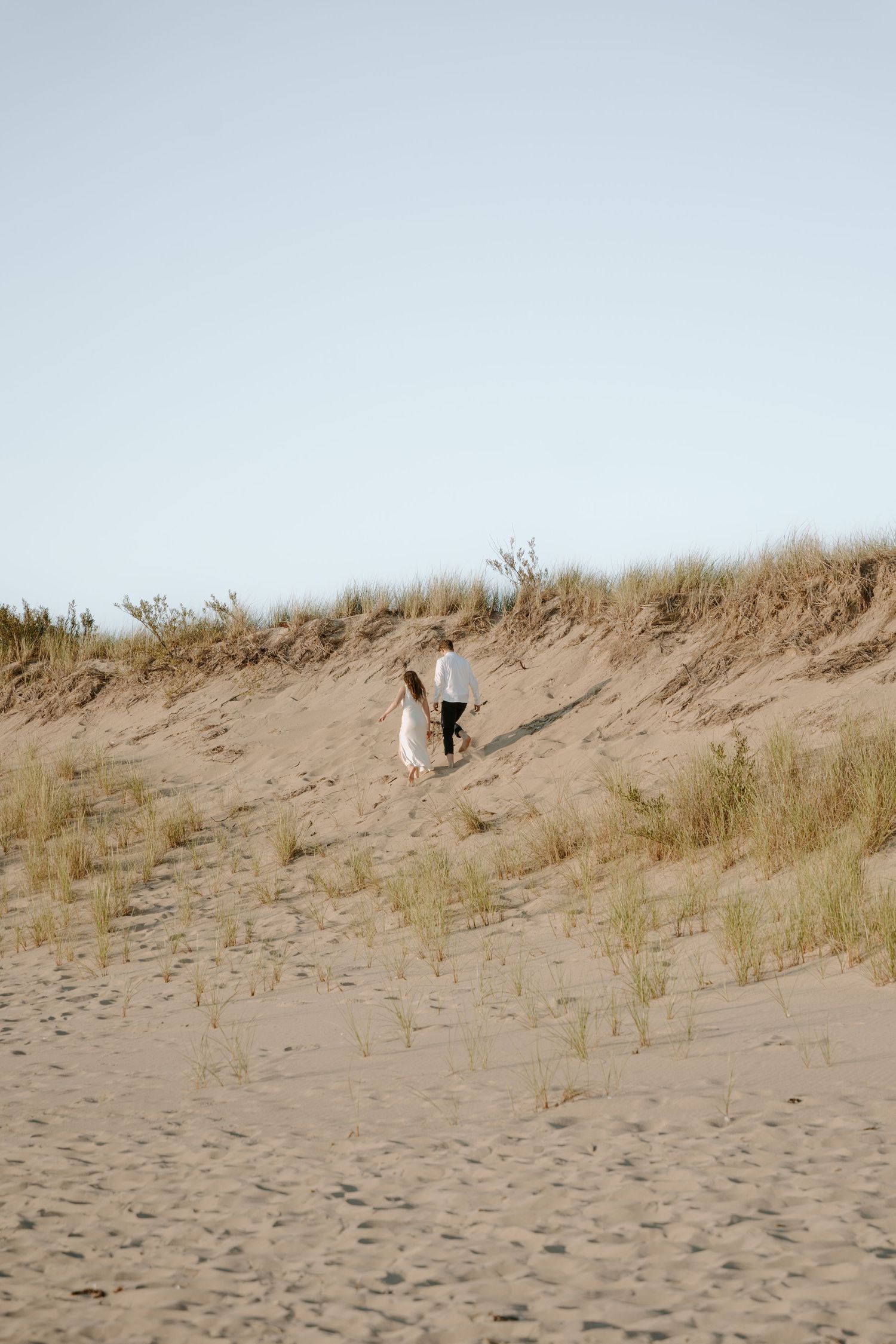 Sandy beach dunes with scattered grass against a pale blue sky.