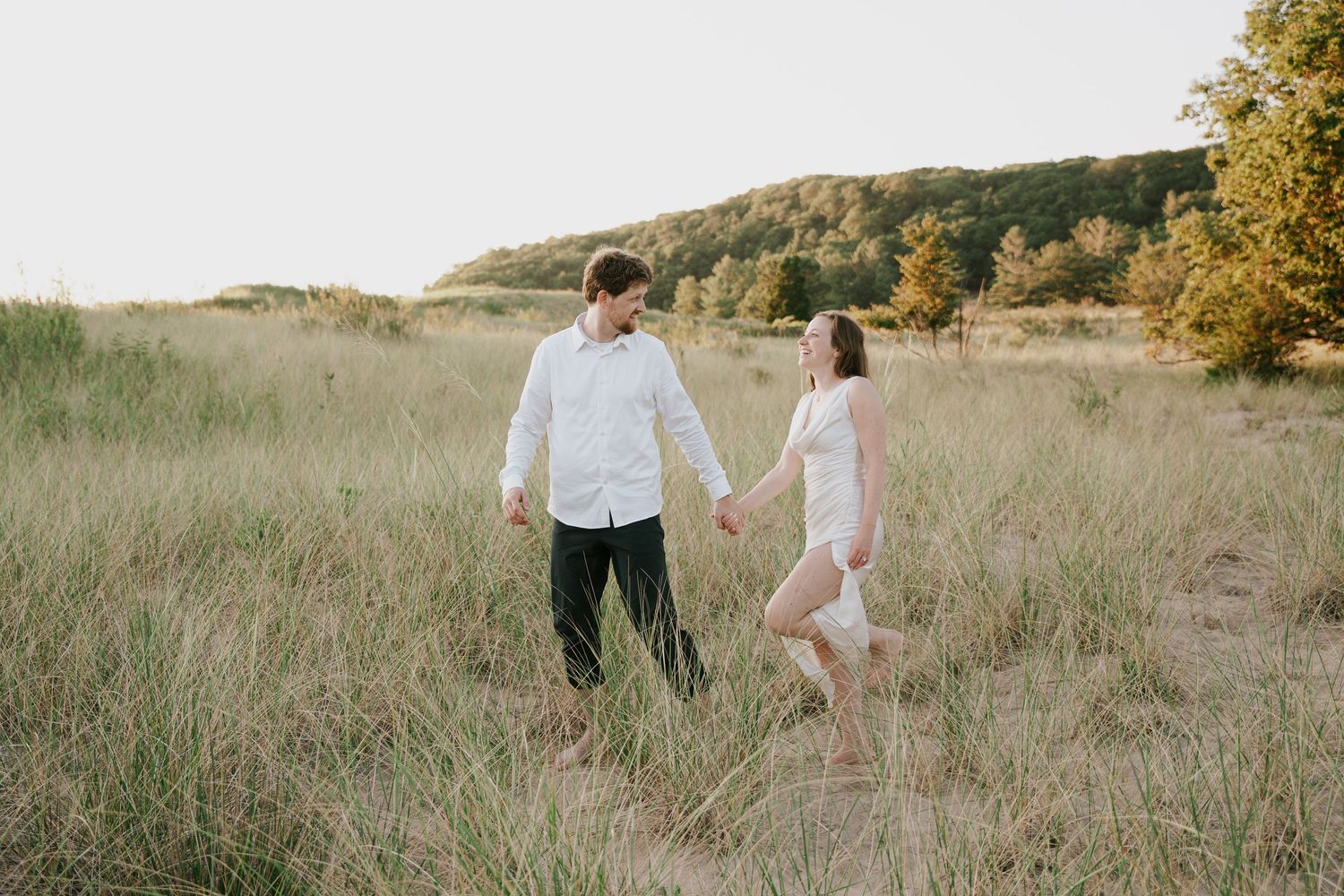 A couple explores a grassy hillside during golden hour, surrounded by natural beauty.