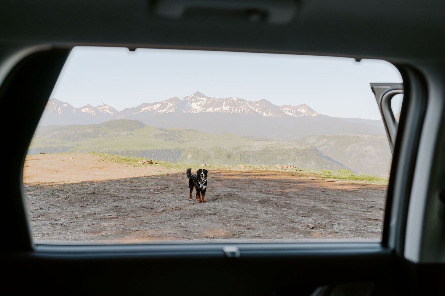 Scenic mountain landscape viewed through a car window showing snow-capped peaks in the distance.