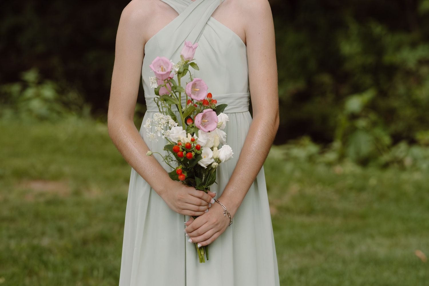 Row of bridesmaids in pale mint dresses holding small floral bouquets.