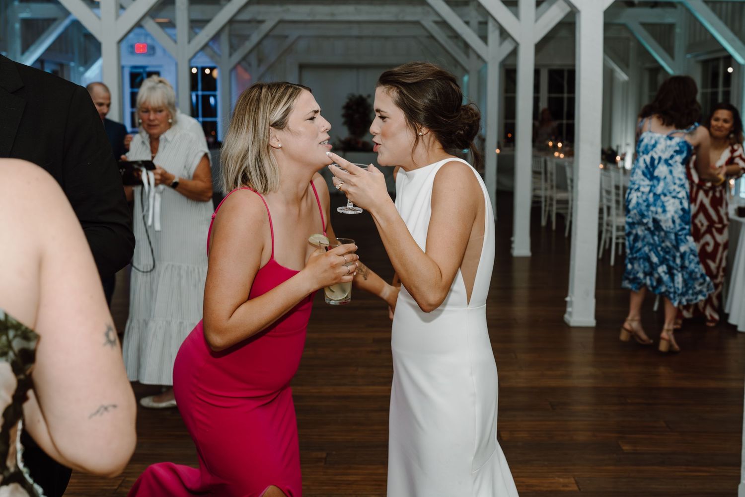 Wedding guests dance and socialize at a reception with white architectural beams.