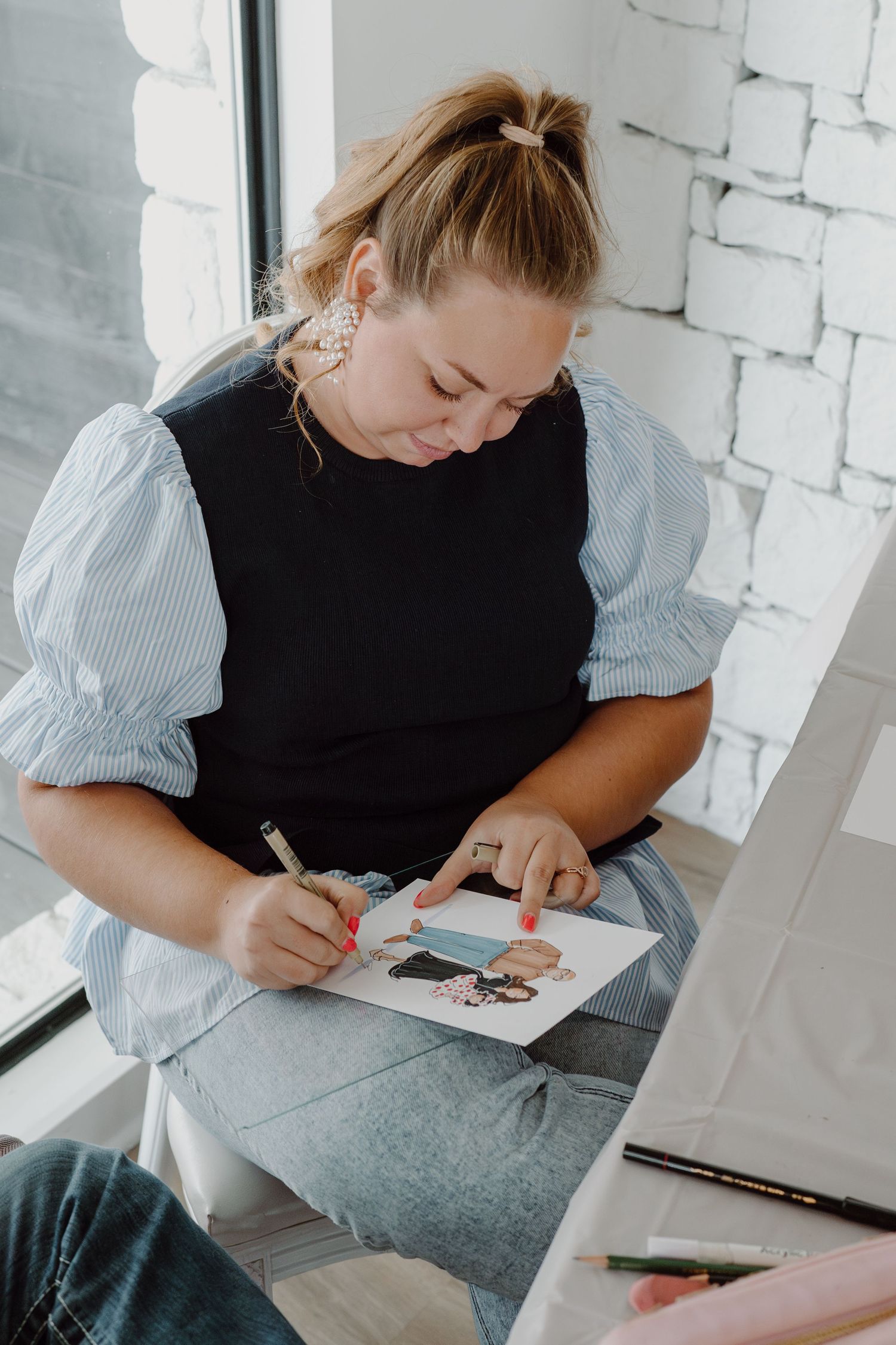 A person in black and striped sleeves working on artwork at a desk.