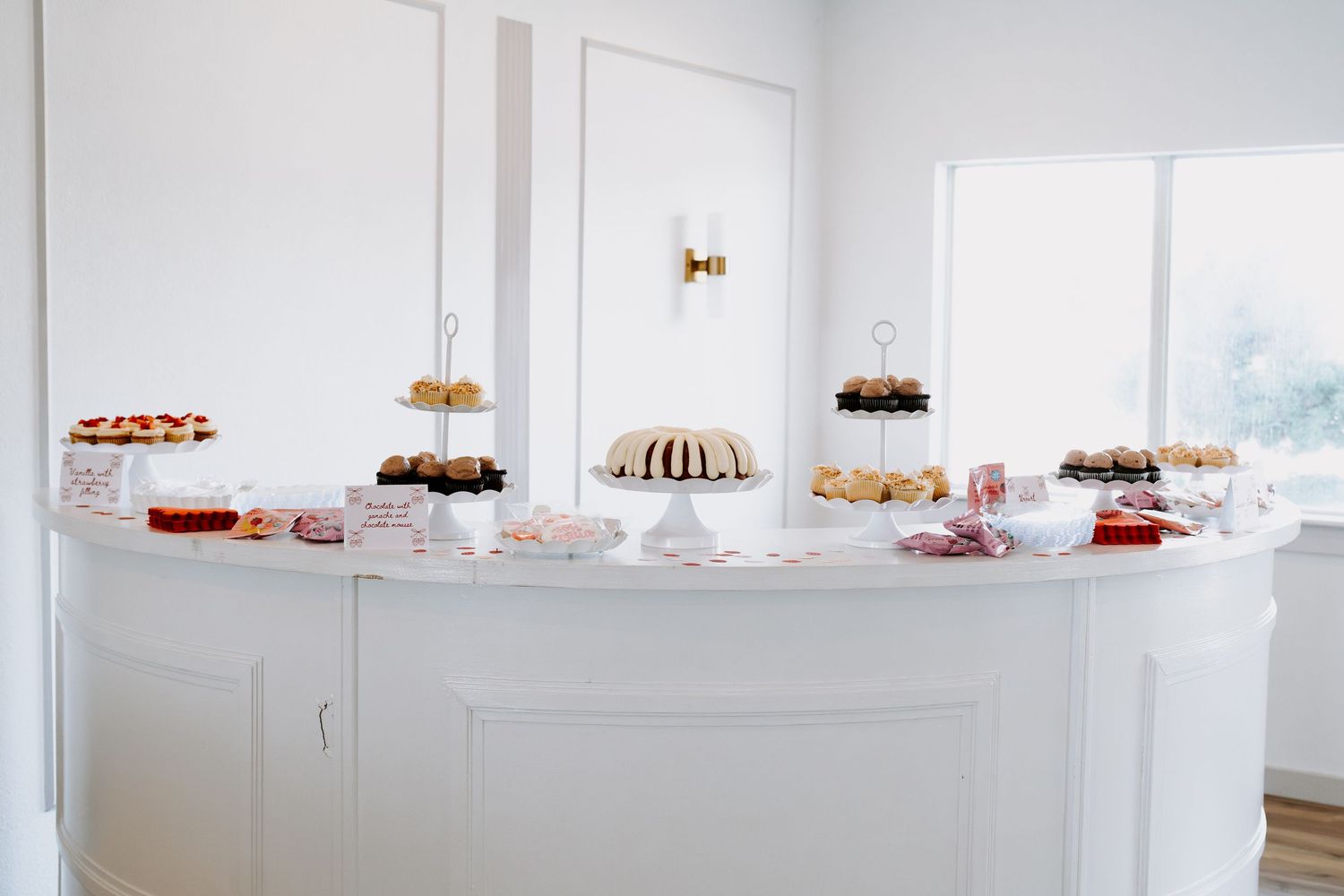White modern event space with desserts displayed on shelves along the wall.