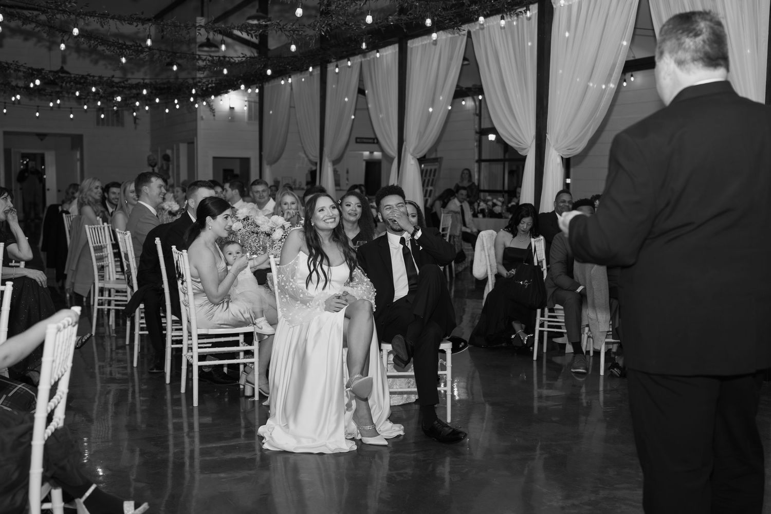 Wedding reception space with industrial-chic decor featuring string lights and exposed ceiling beams.