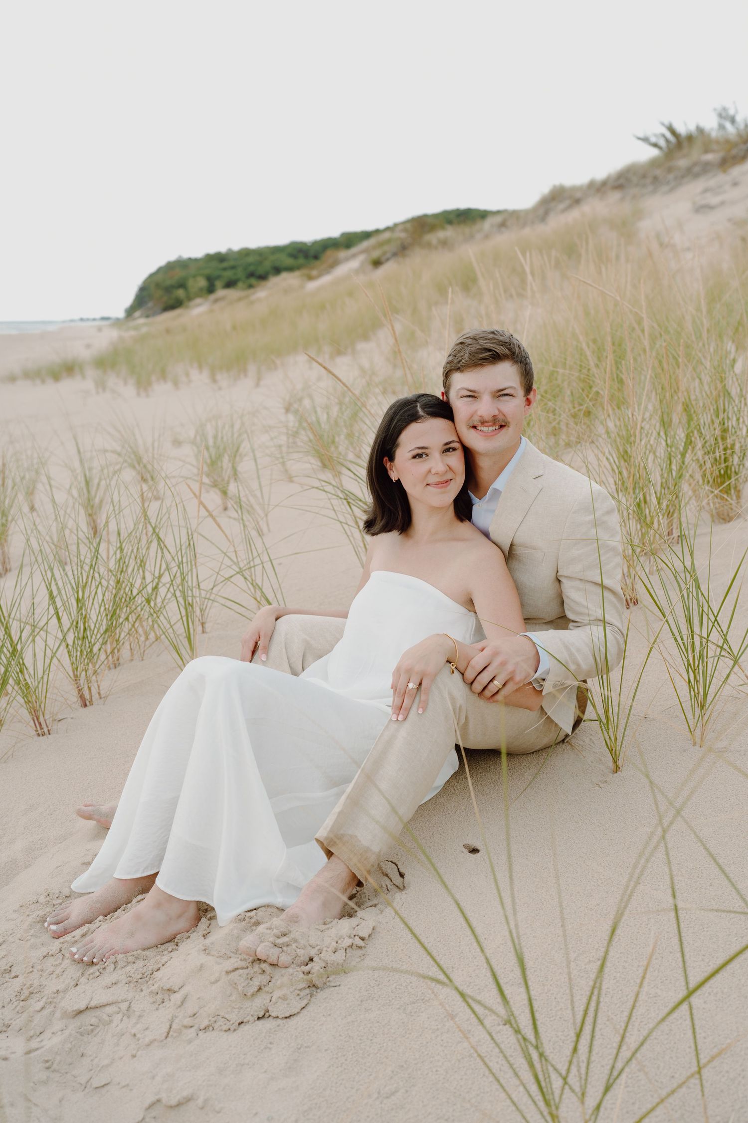 Couple in wedding attire sharing tender moments on coastal sand dunes.