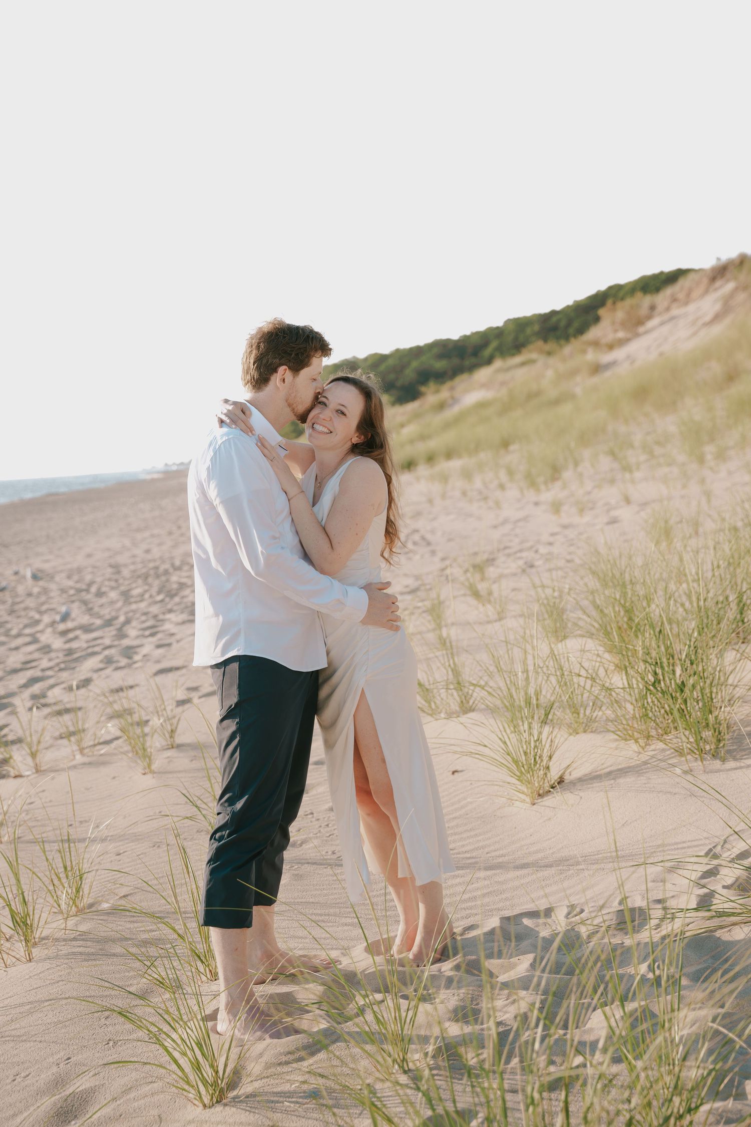 A loving embrace captured against a backdrop of coastal dunes and beach grass.