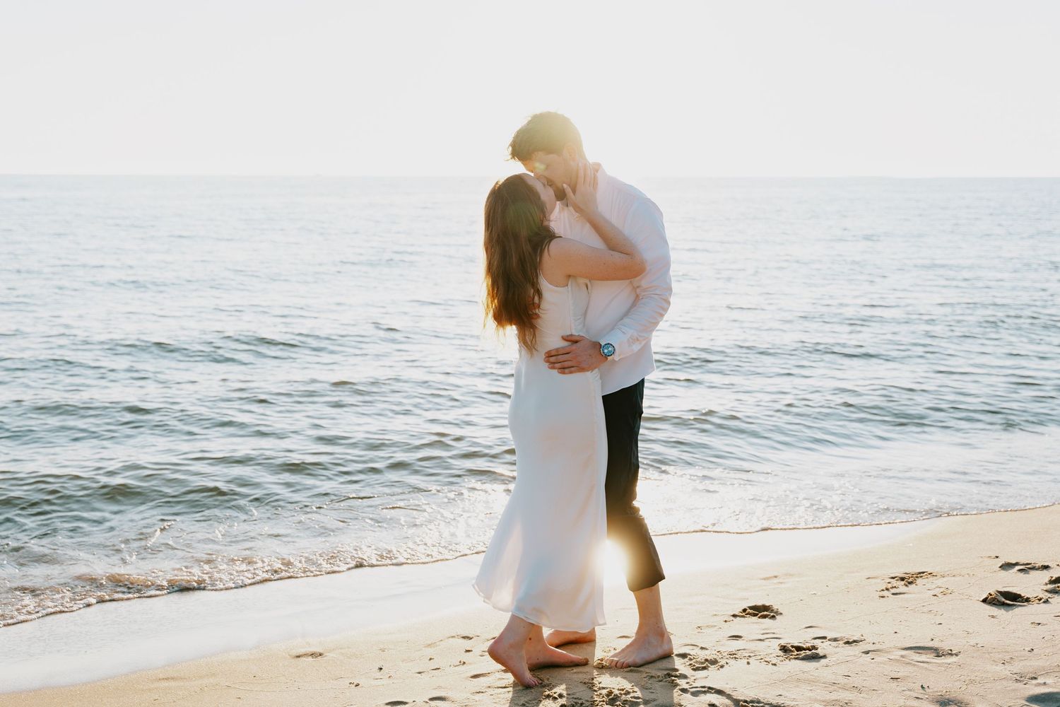 Couple in white and black attire embracing on sunny beach.