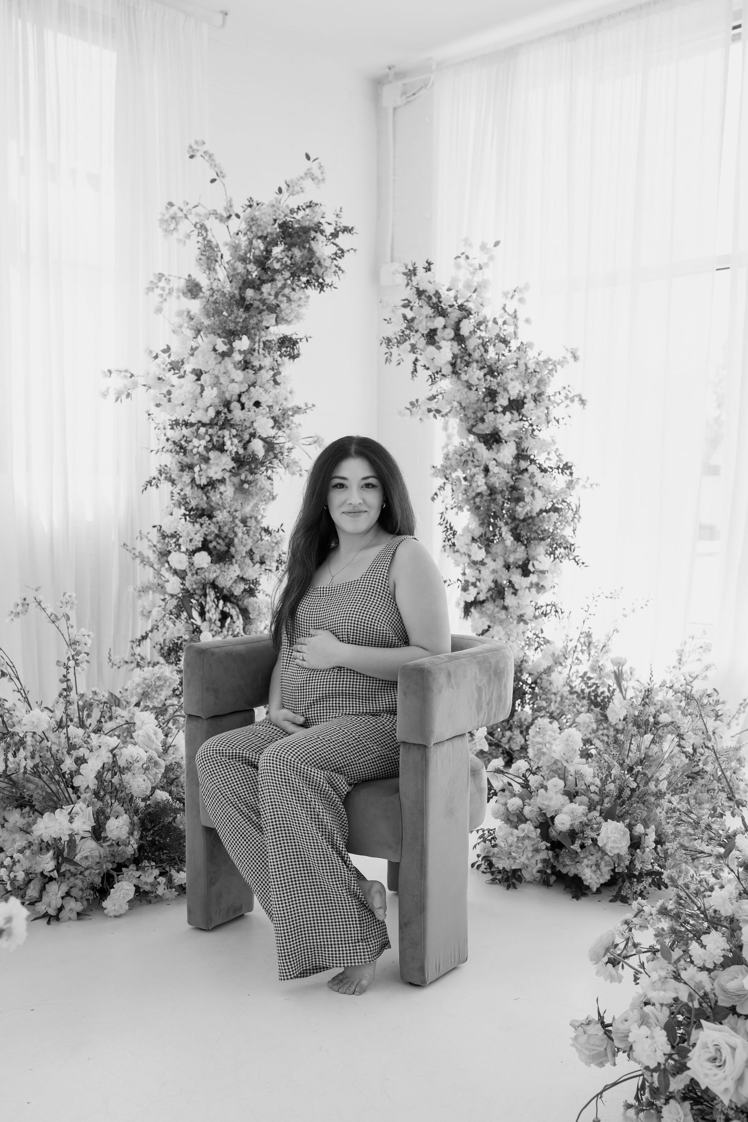 Black and white maternity portrait with woman seated against floral backdrop.