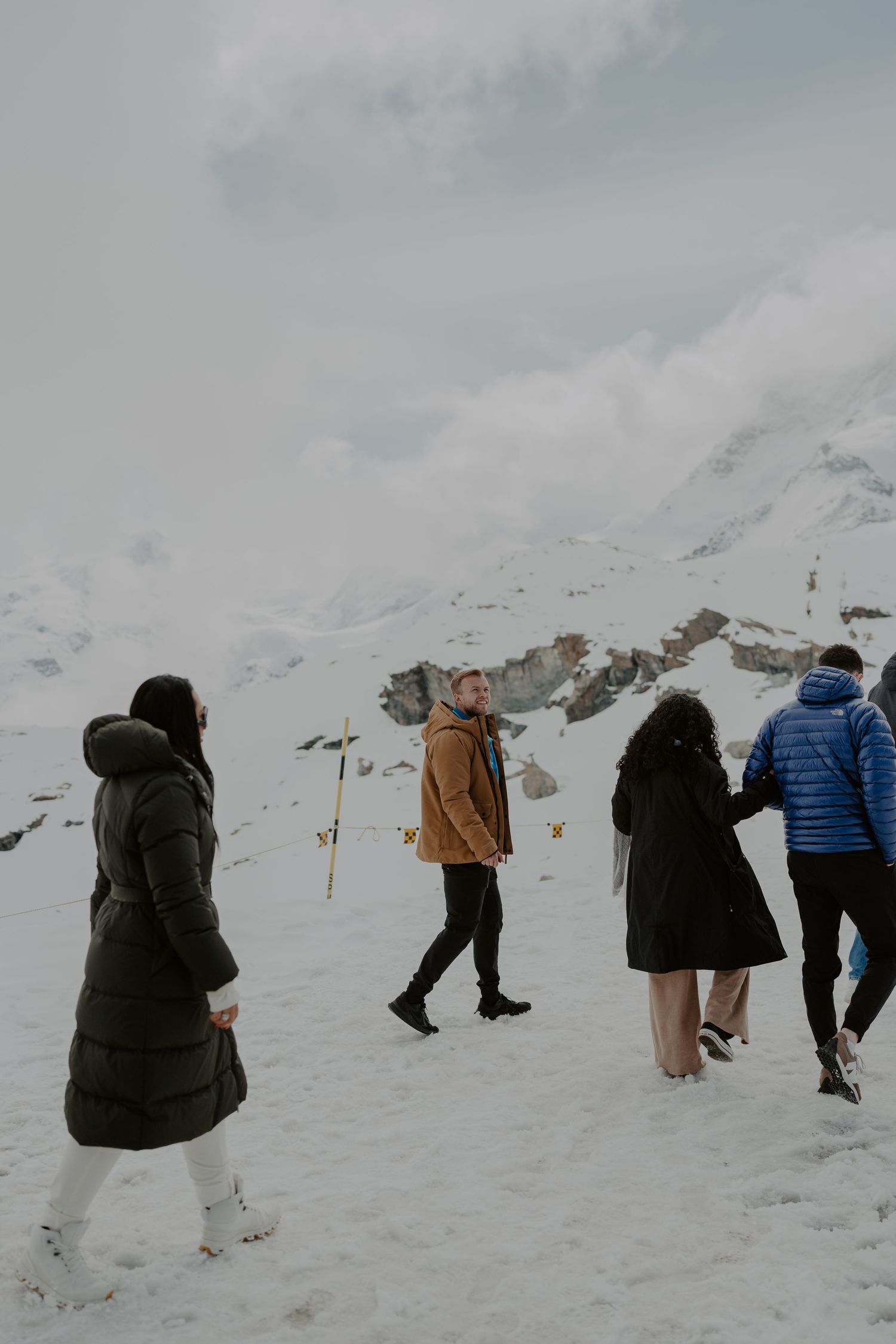 Group of people walking through snowy mountain terrain with ski poles.