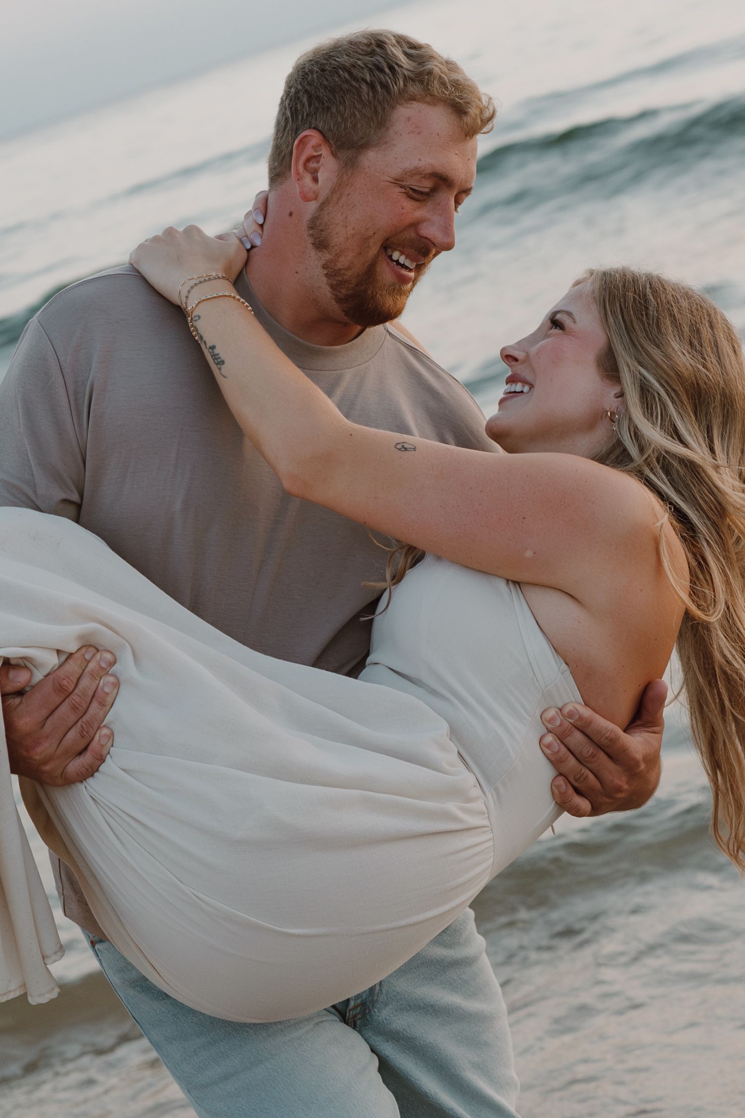 A couple shares an intimate moment on the beach with waves crashing behind them.