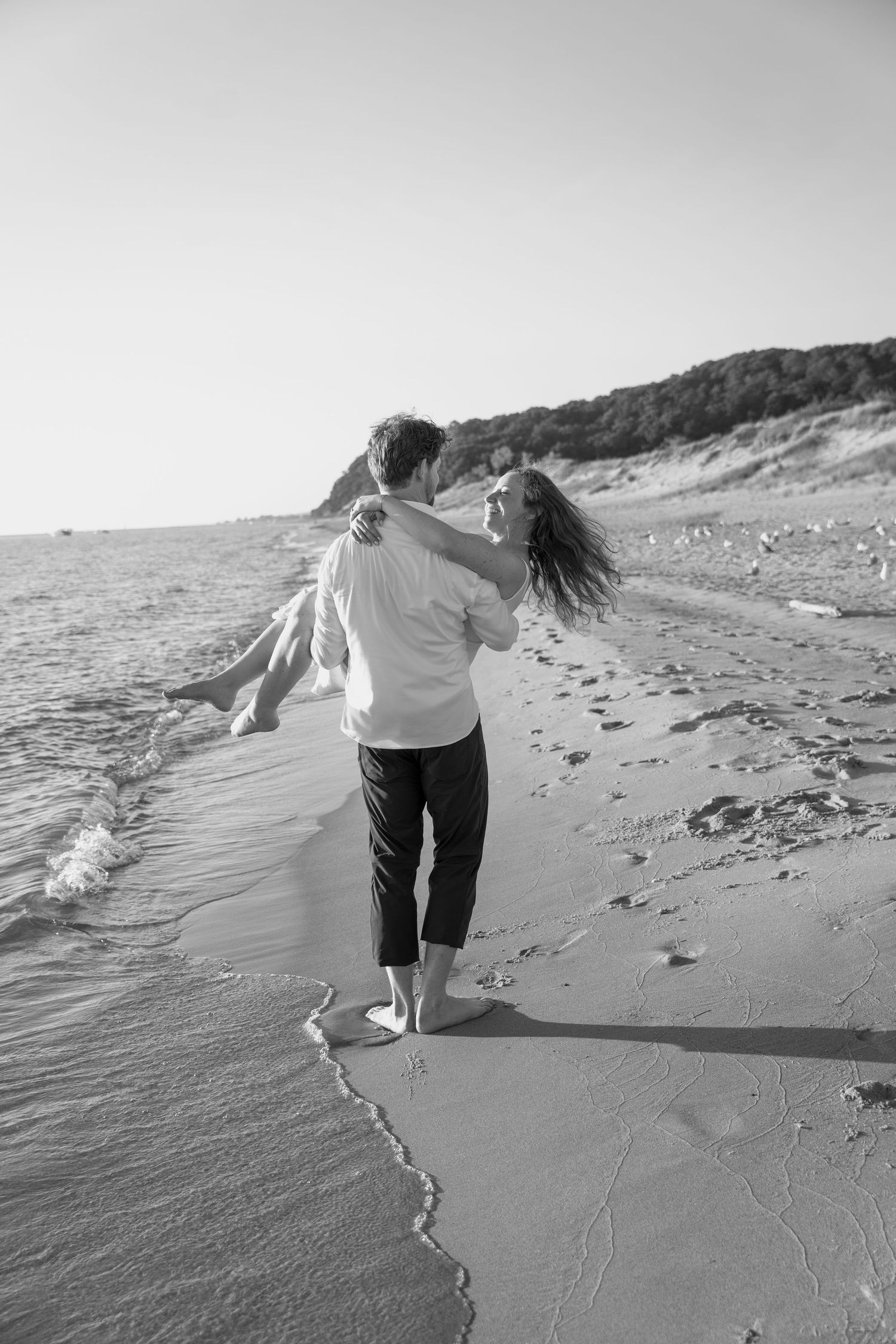 Black and white coastal portrait of couple dancing by the waves.