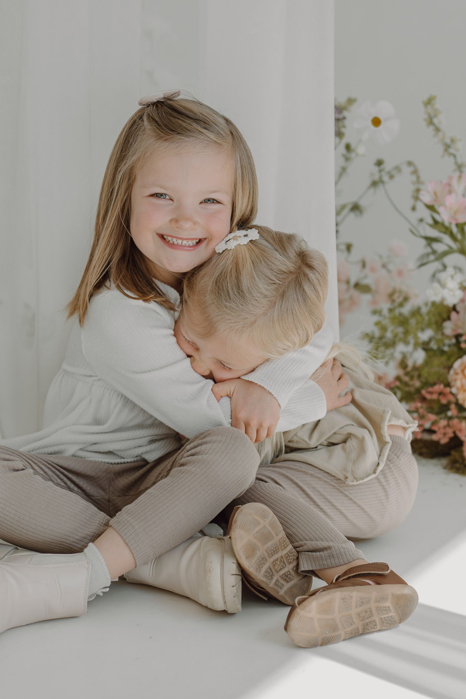 Two young children share sweet embrace while sitting on white floor.