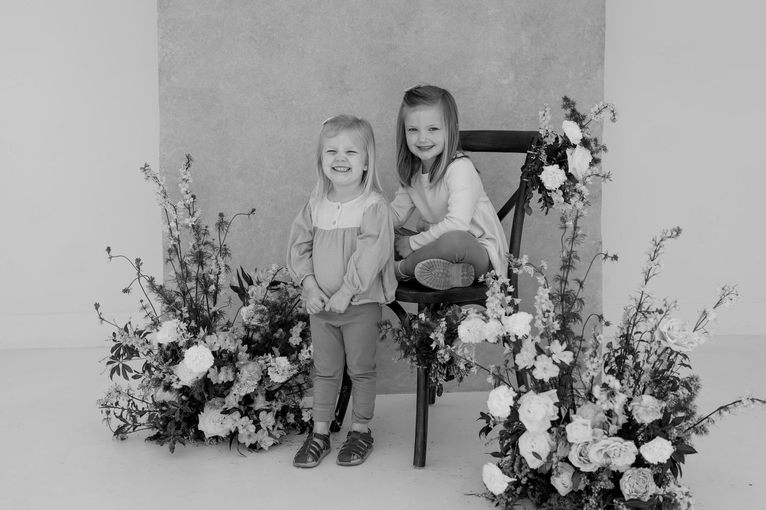 Studio photography scene with delicate floral arrangements and wooden chair against light background.