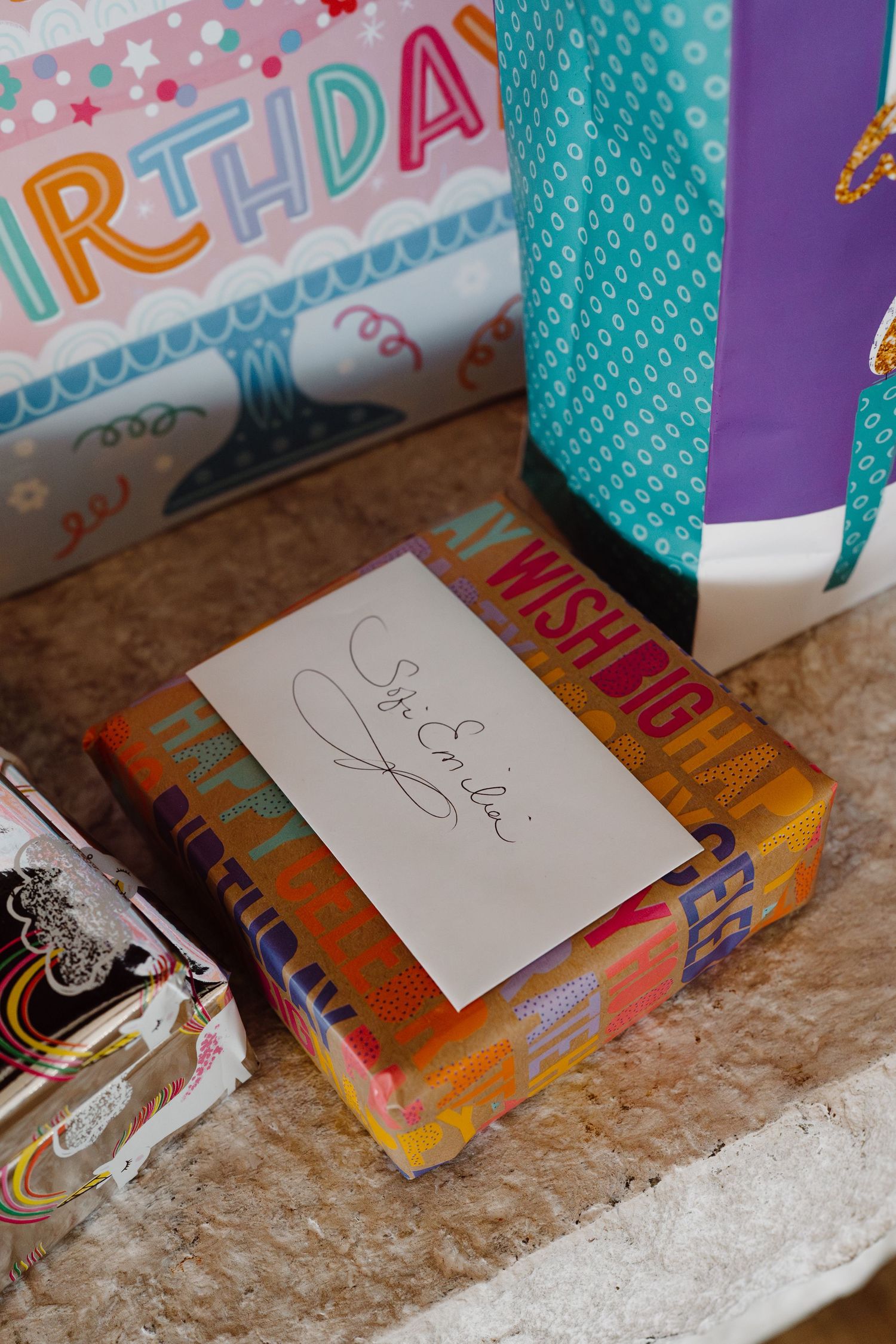 Birthday cards and gifts arranged on a stone mantel with colorful wrapping paper.