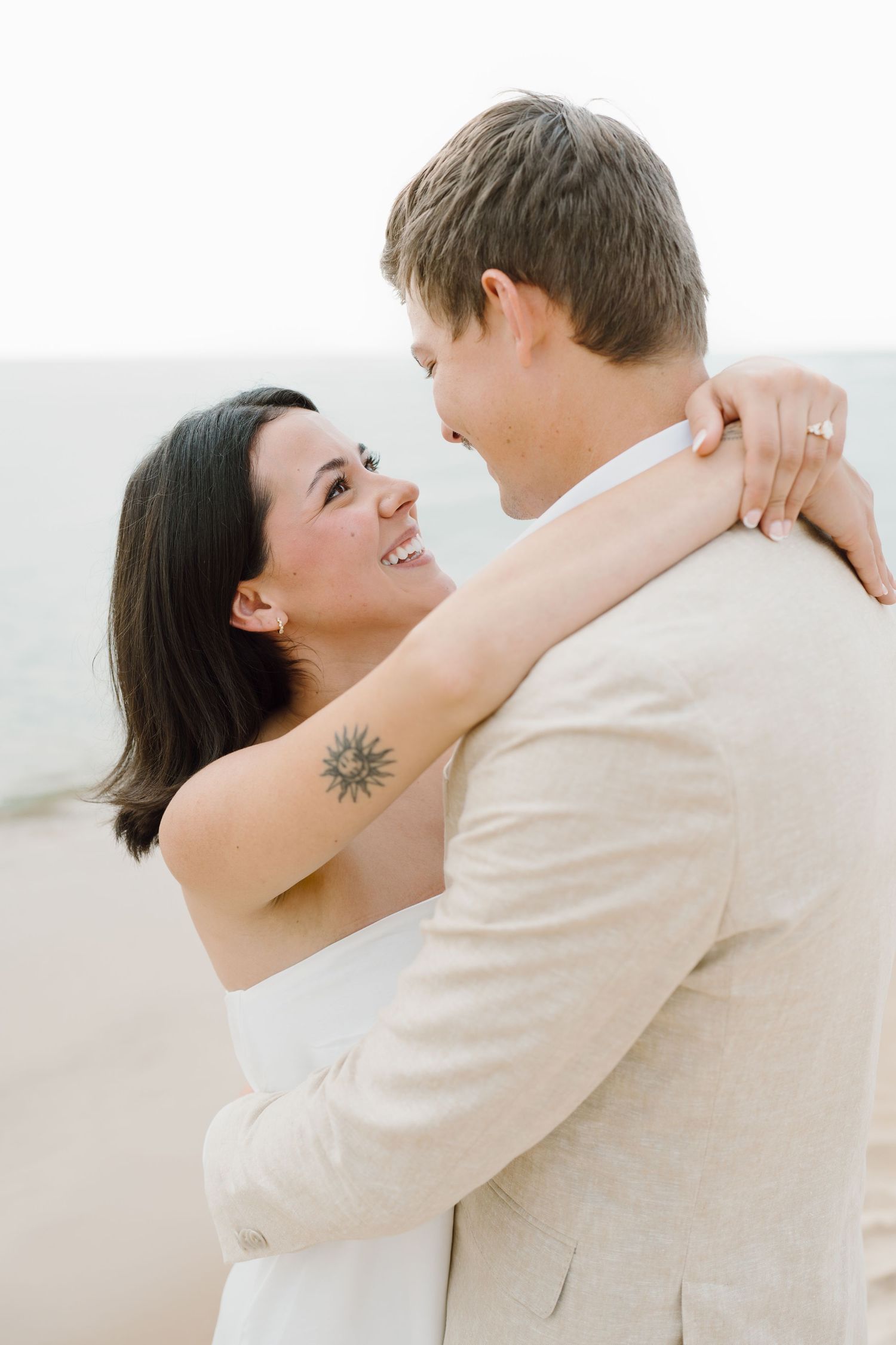 Close-up beach portrait of couple in light colored clothing sharing tender moment.