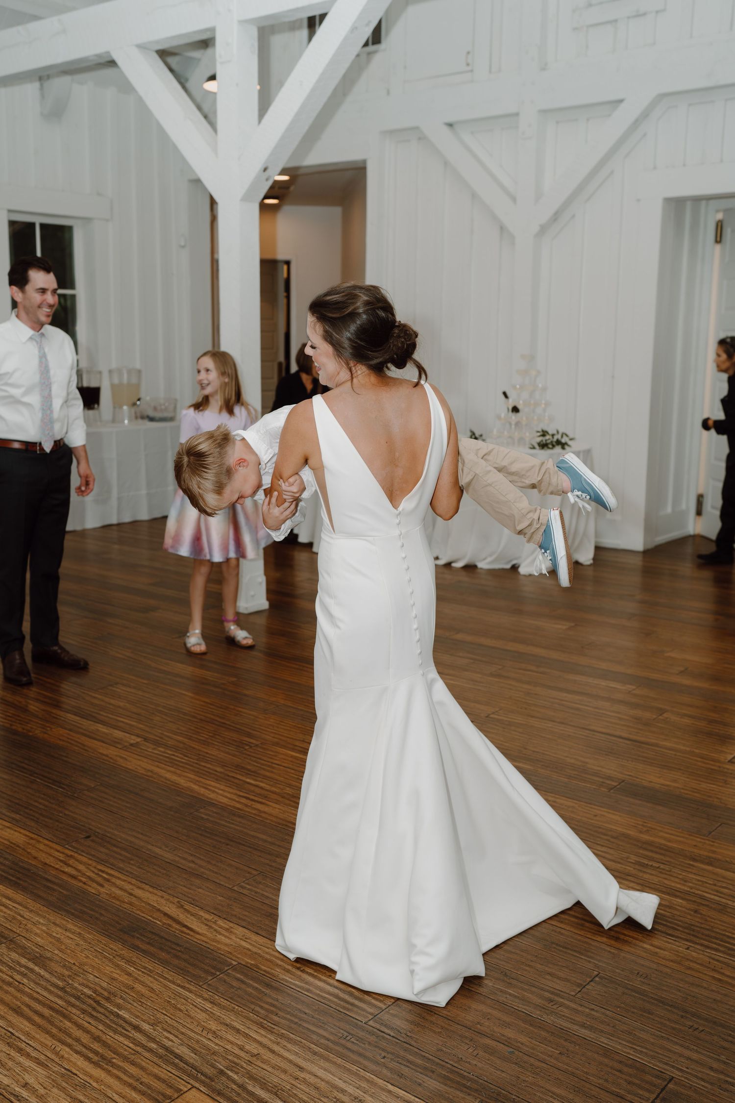 Wedding guests dancing and celebrating on a polished hardwood floor in an elegant white venue.