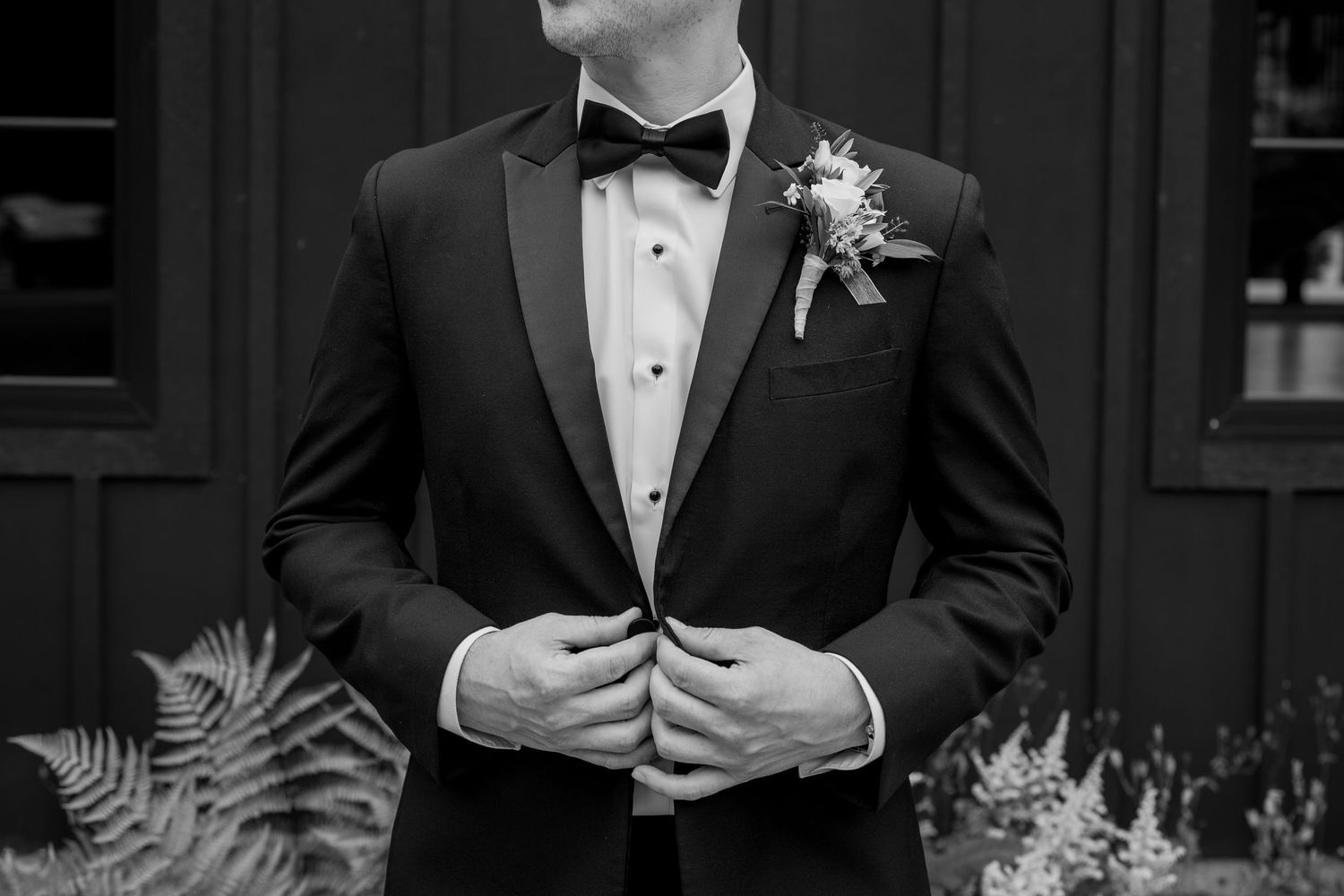 Elegant tuxedo detail shot with boutonniere against dark exterior wall.