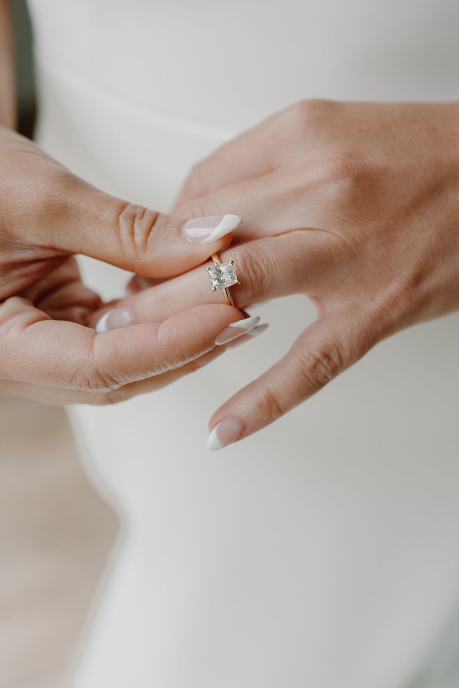 Close-up shots of an elegant diamond engagement ring on a hand with neutral manicured nails.