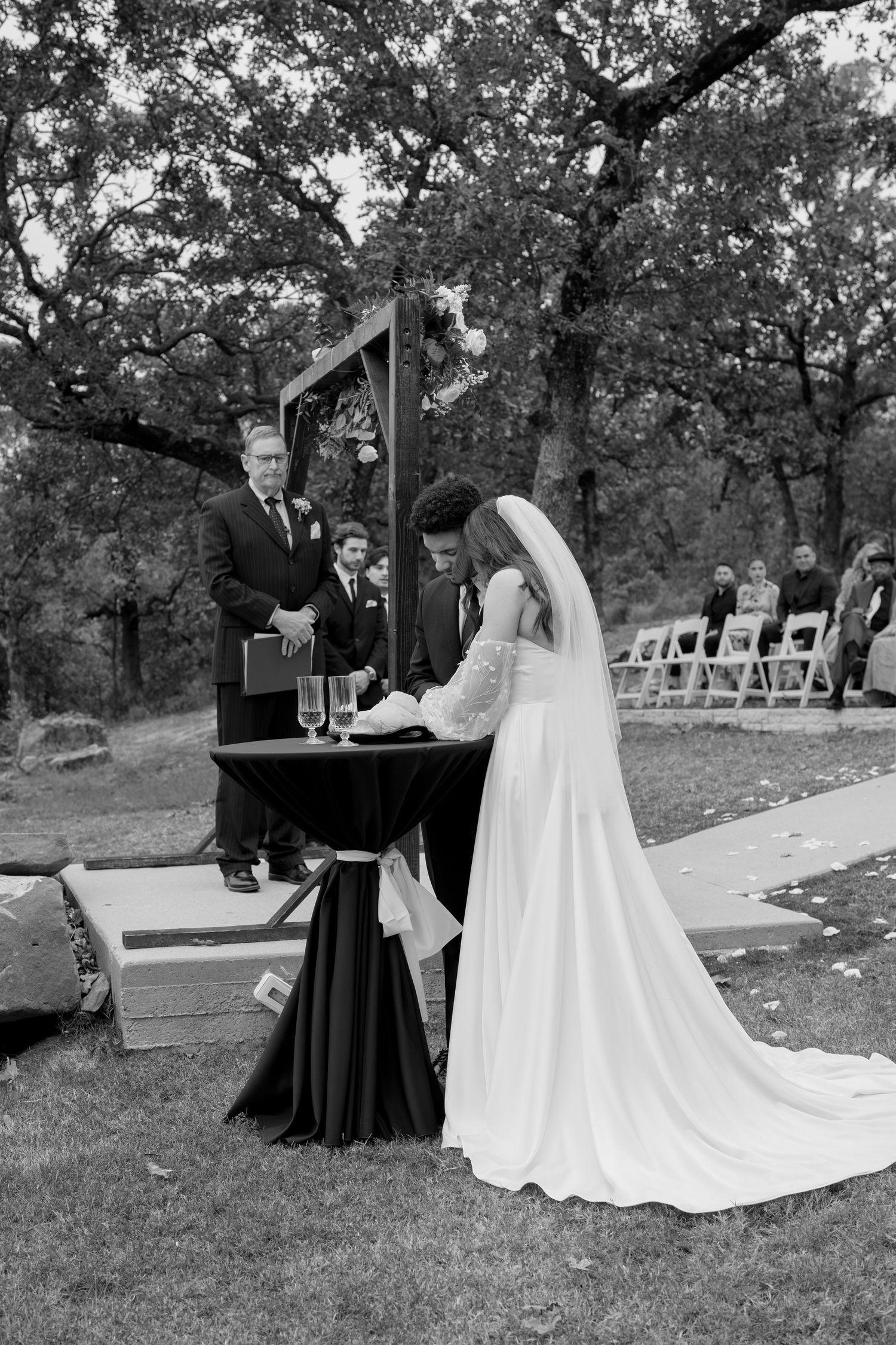 Wedding party gathered on stone pathway during outdoor ceremony with long white dress train visible.