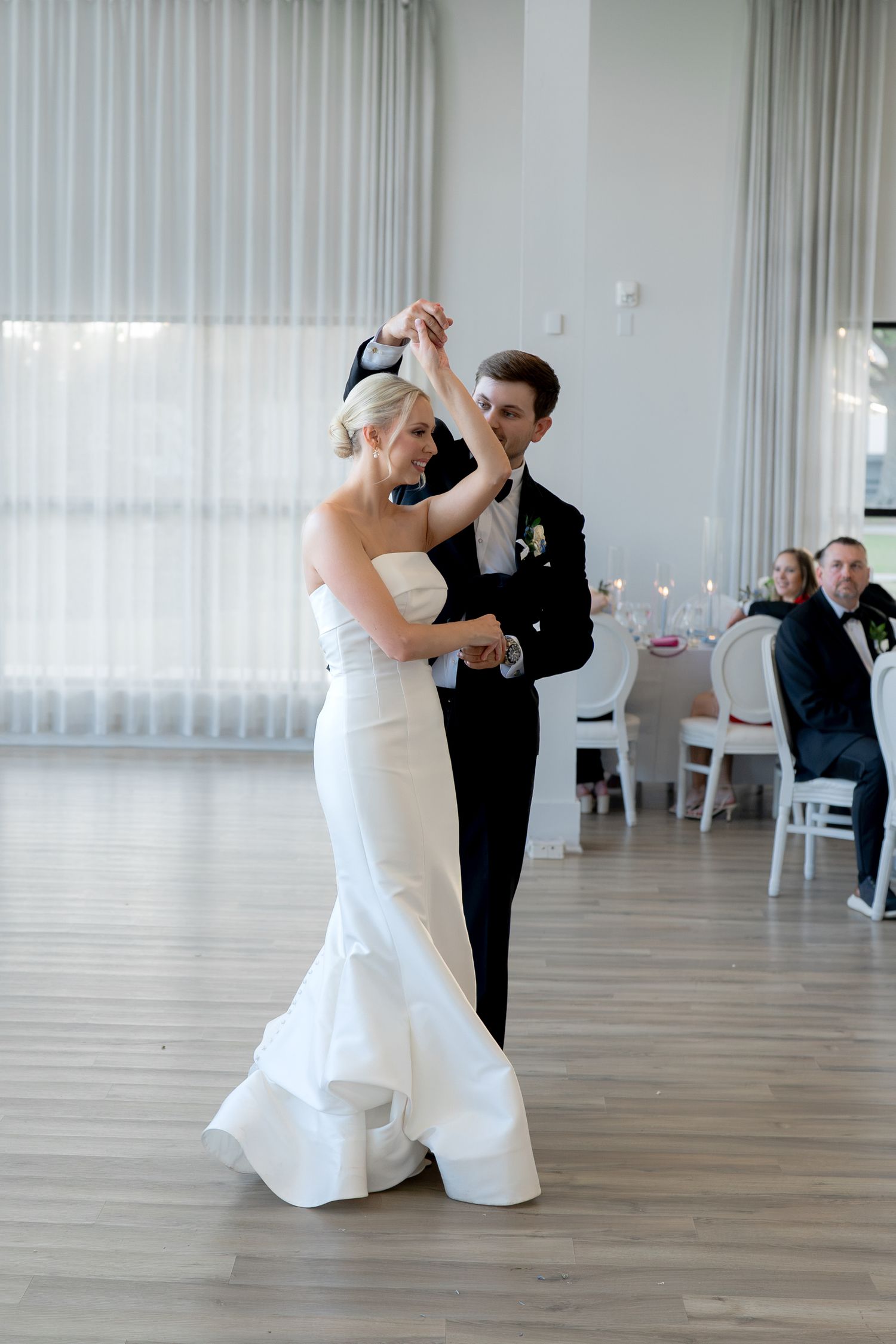 Bride and groom share their first dance in an elegant white ballroom during a wedding reception.