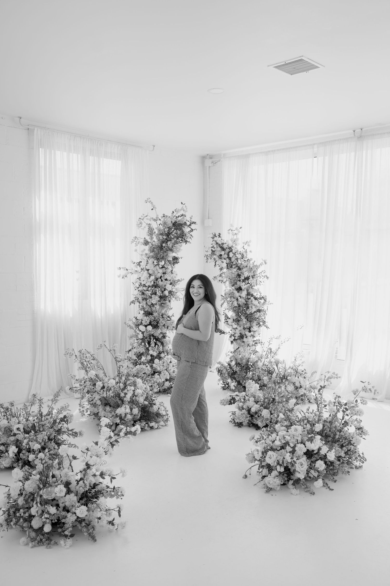 Black and white maternity portrait with floral arch and elegant studio backdrop.