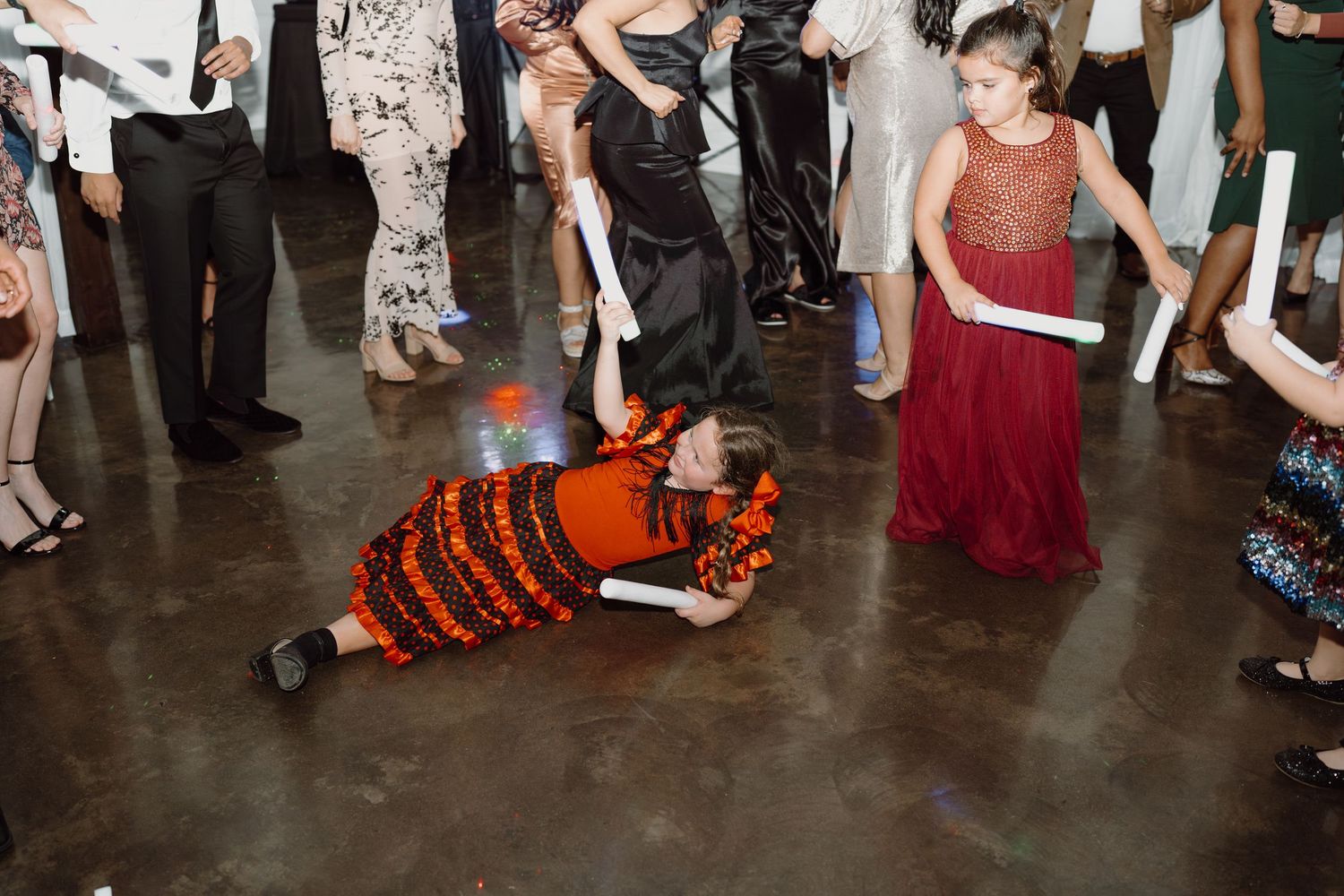 Wedding party guests dancing and celebrating on a concrete floor at an indoor venue.
