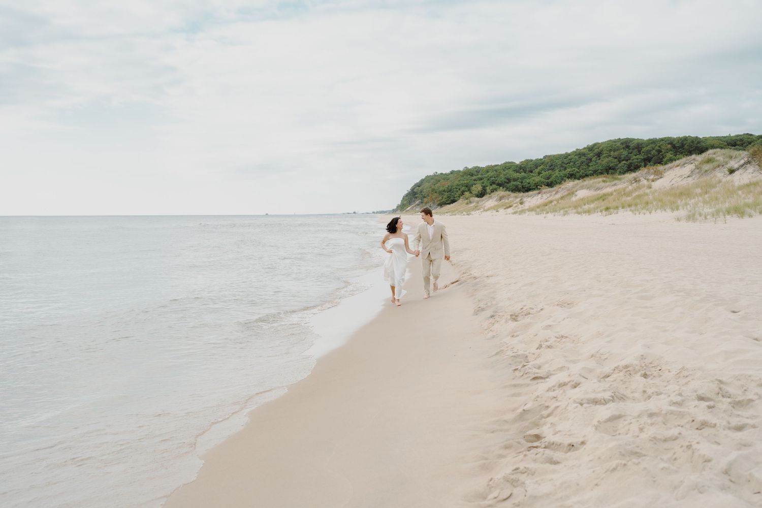 Panoramic view of a pristine beach with gentle waves and tree-covered cliffs in the distance.