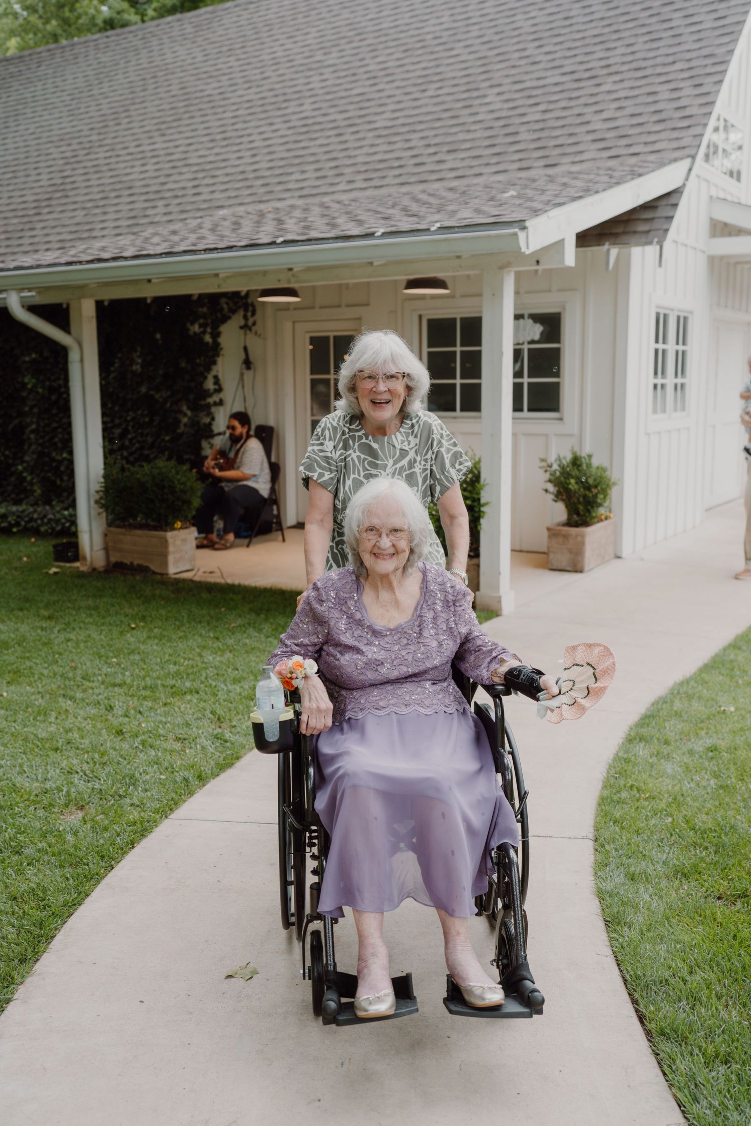 Person in wheelchair wearing purple dress smiles outside white building with covered porch.