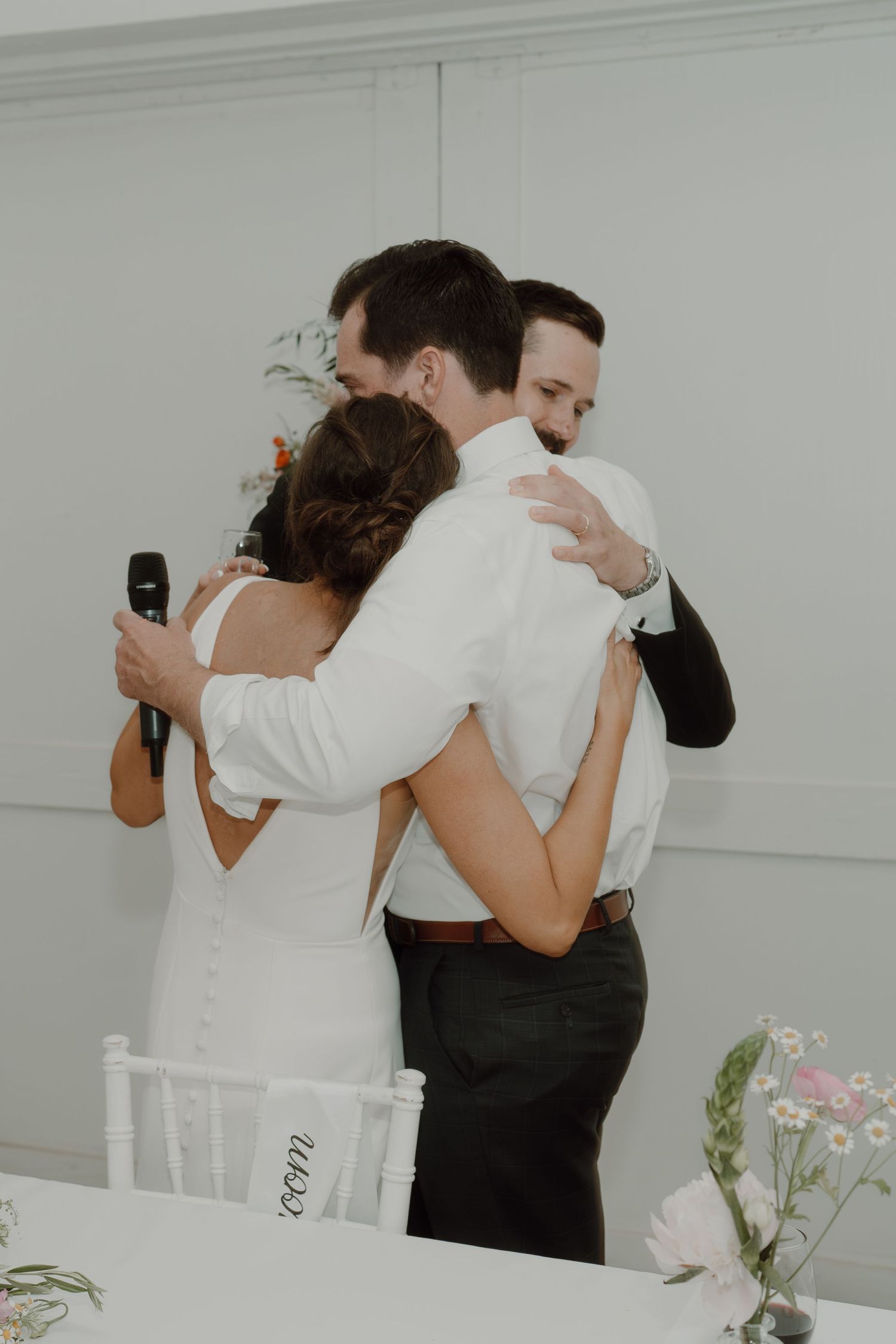Wedding guests share candid moments at a white-themed reception venue with floral decorations.