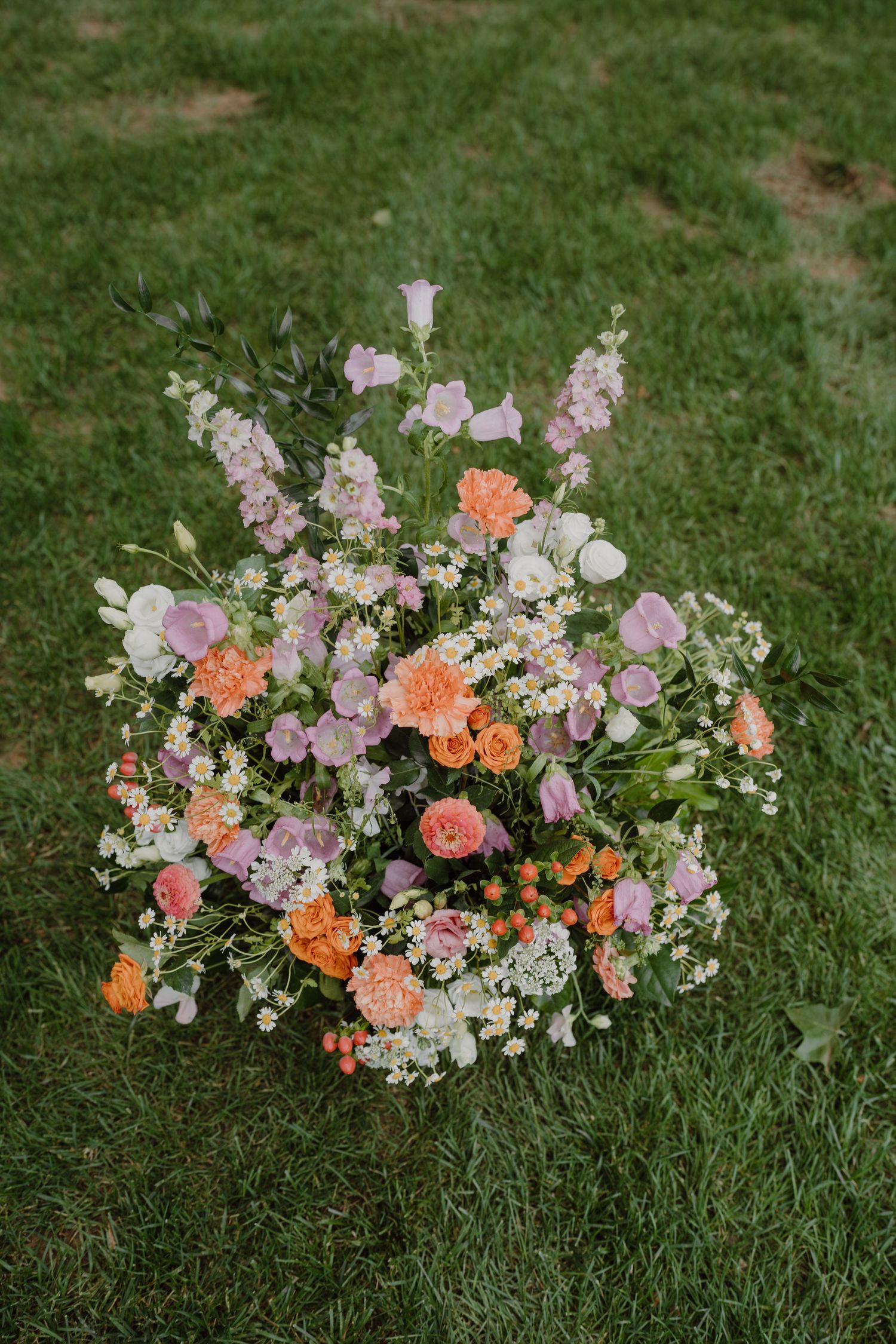 Peach and pink floral arrangement with mixed flowers displayed on grass.