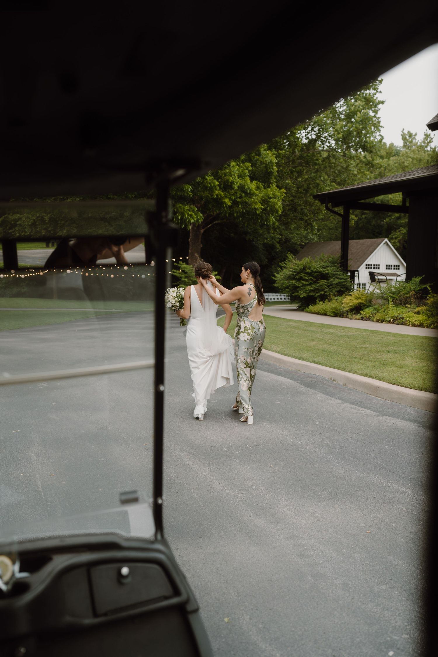 View through a car windshield of people walking on a paved driveway.