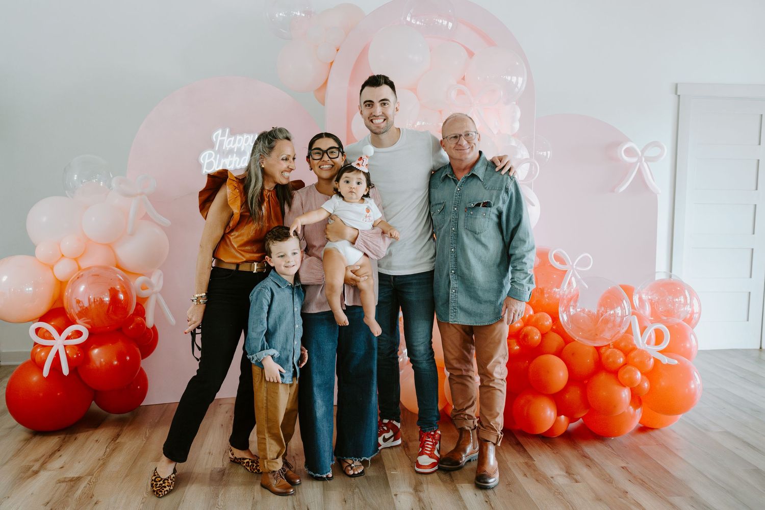 Group photo against a festive balloon backdrop in shades of pink and orange.