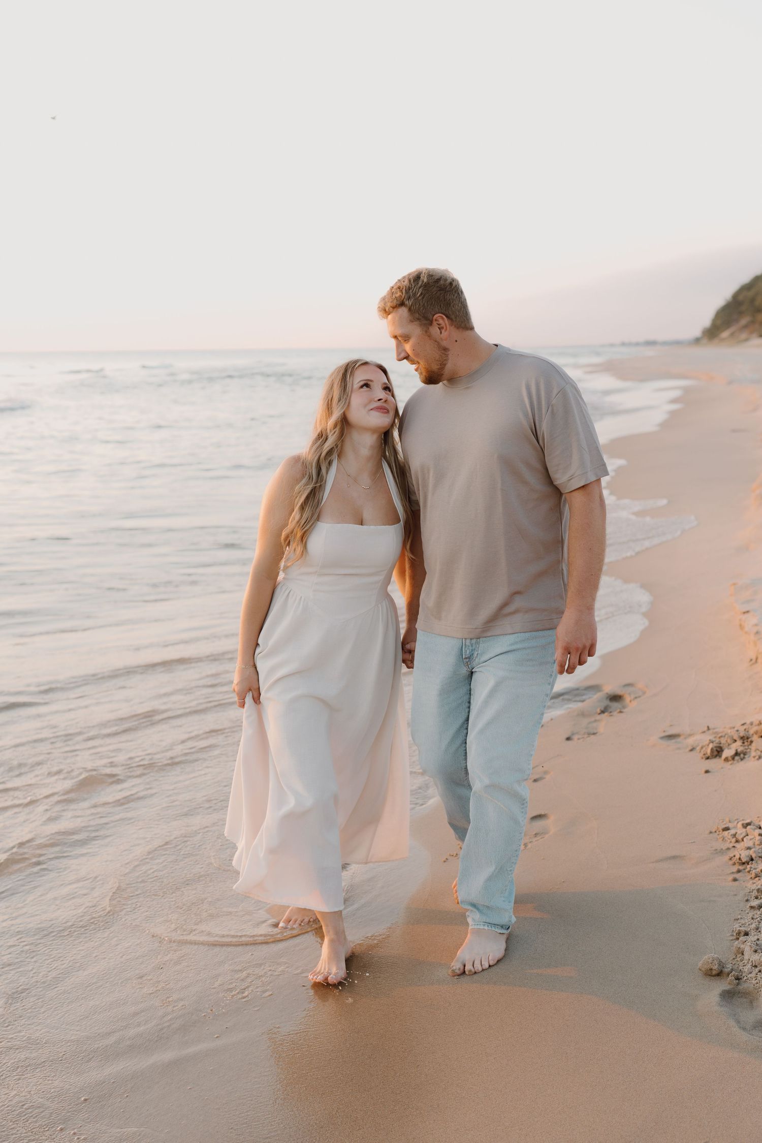 Two people stroll barefoot together on a peaceful sandy beach during golden hour.