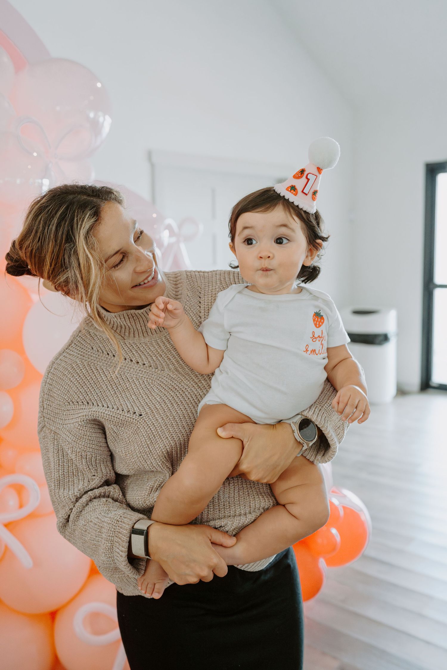 A sweet moment captured in a bright room decorated with peach and white balloons.