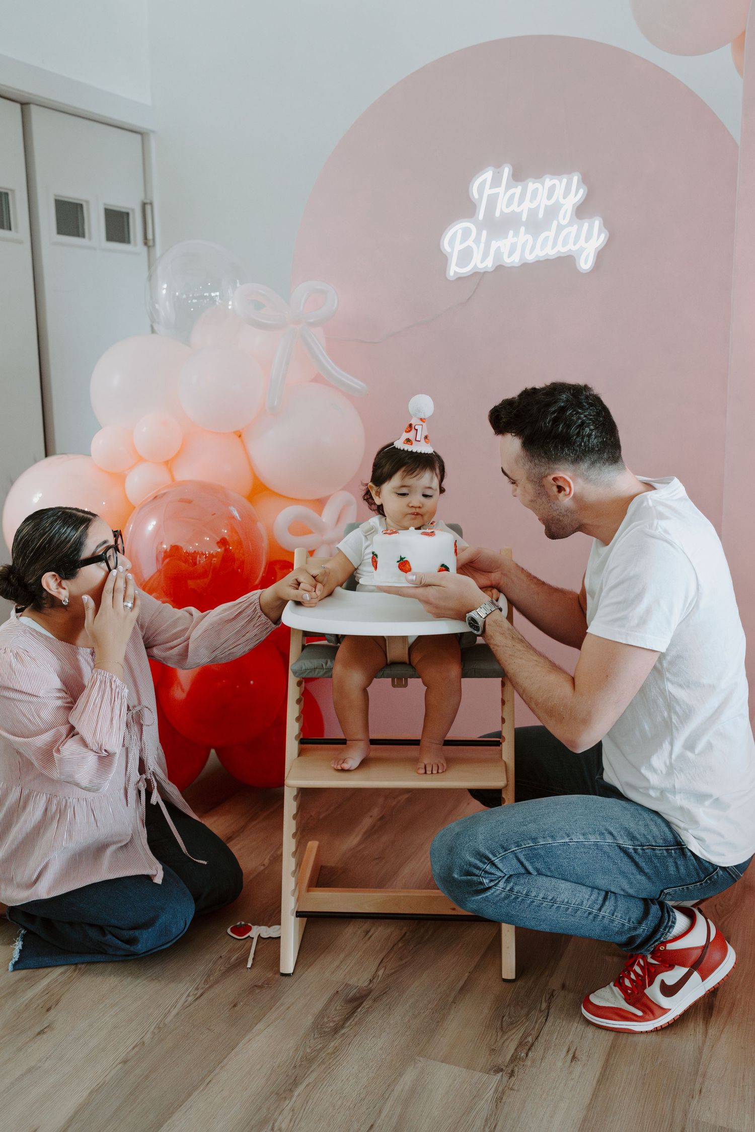 Candid family birthday celebration with pink balloons and neon sign creating festive atmosphere.