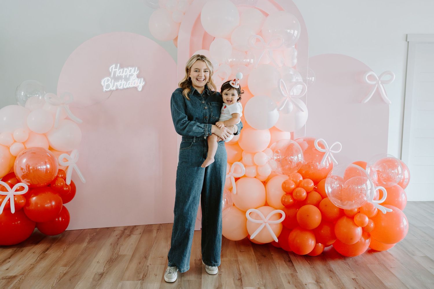 Minimalist birthday backdrop with peach and coral balloon arrangement against white wall.