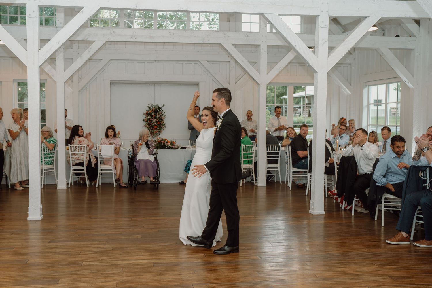 Wedding reception dance floor scene in a rustic white barn with exposed beams.