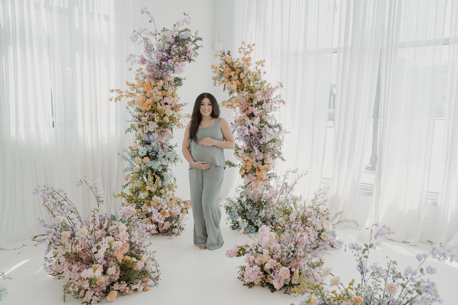Studio maternity photography with dramatic floral arrangements and natural window light.