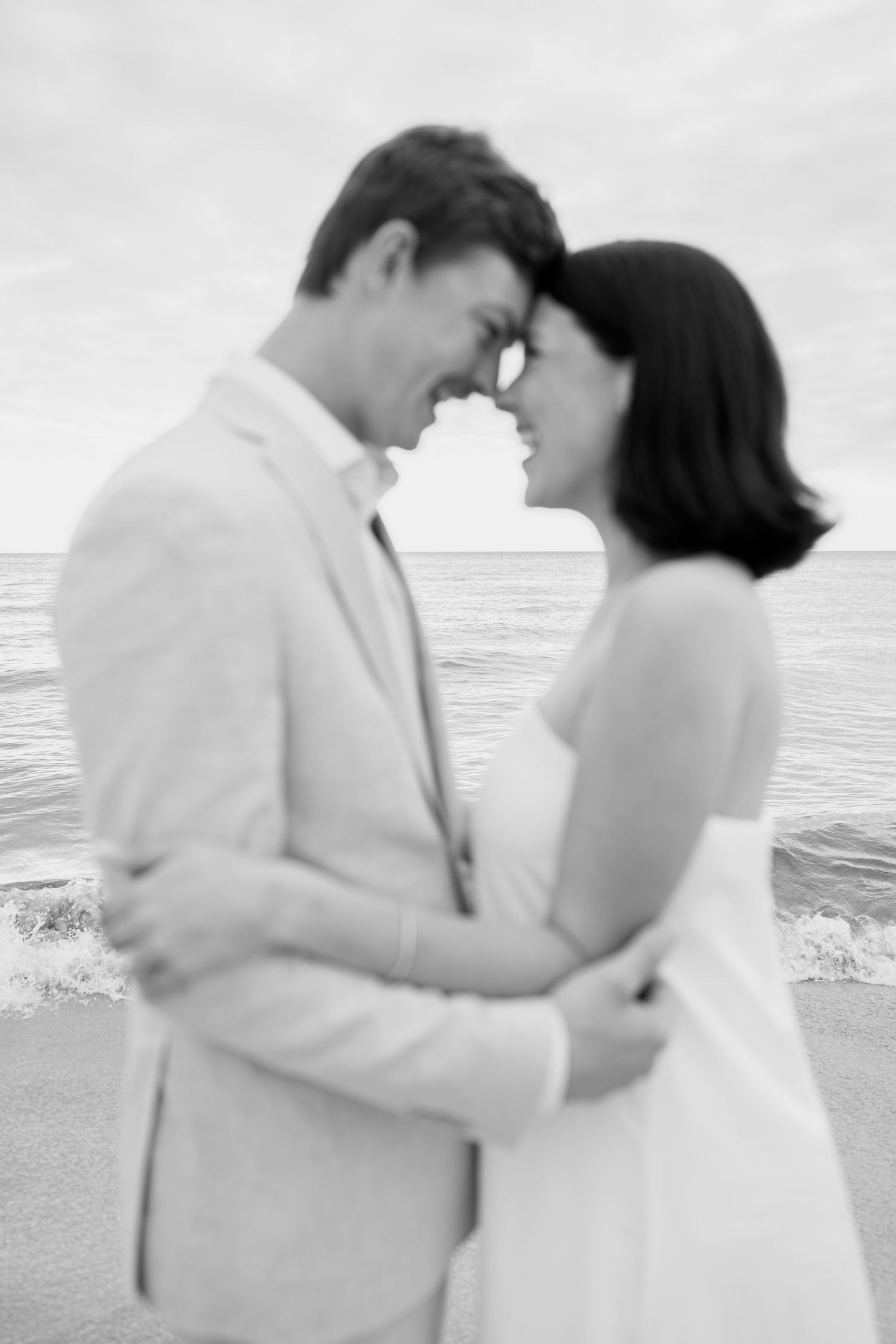 Romantic beach embrace with couple in white and beige attire.