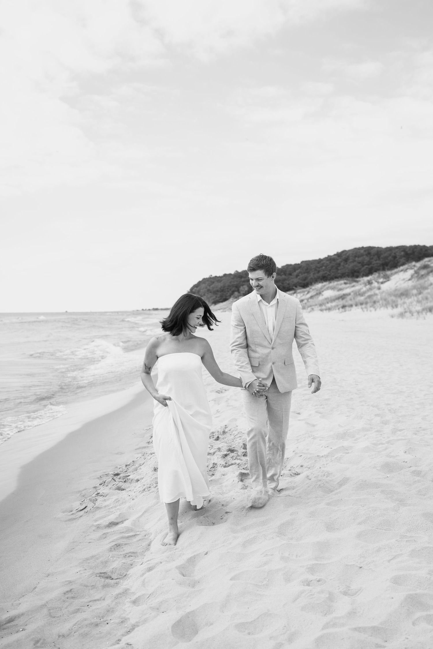 A couple runs playfully along the beach in black and white photography.