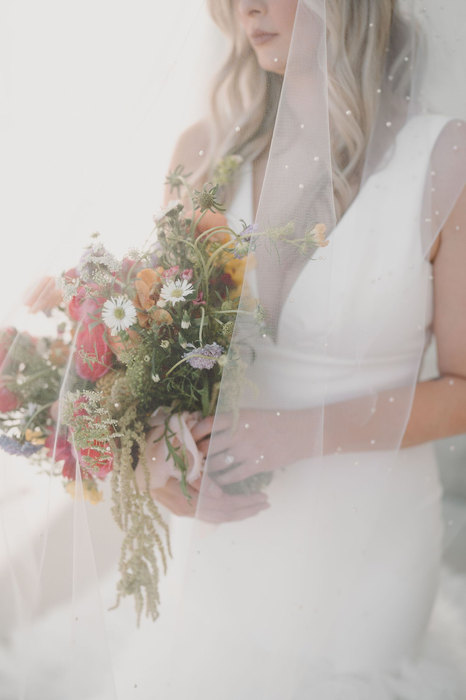 Dreamy bridal portrait with colorful wildflower bouquet and pearl-dotted veil.